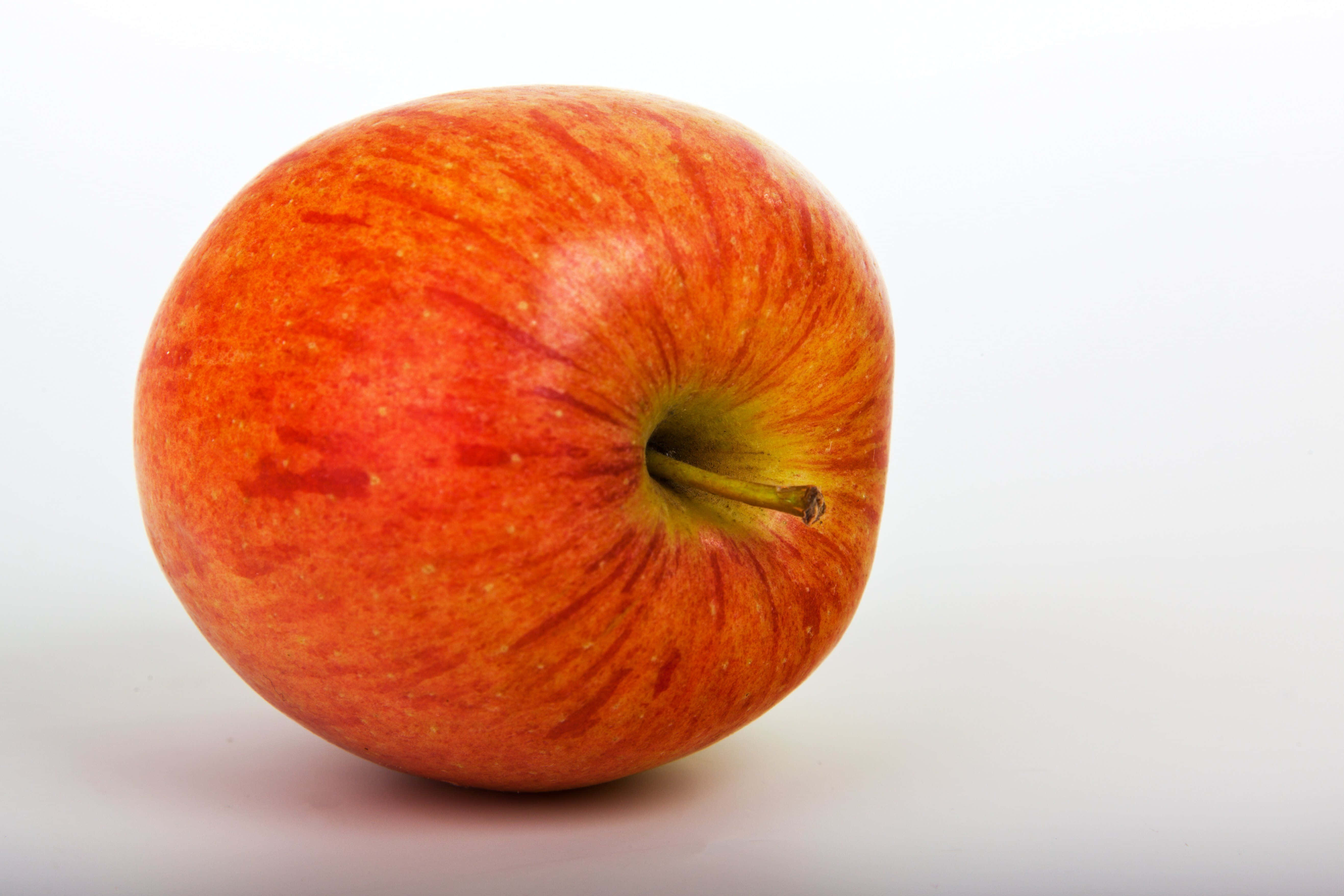 4K Apple 桌布 壁紙 — 一個鮮紅色的蘋果帶有黃色條紋，孤立在潔白的表面上，展示其光澤的果皮和天然的果梗。