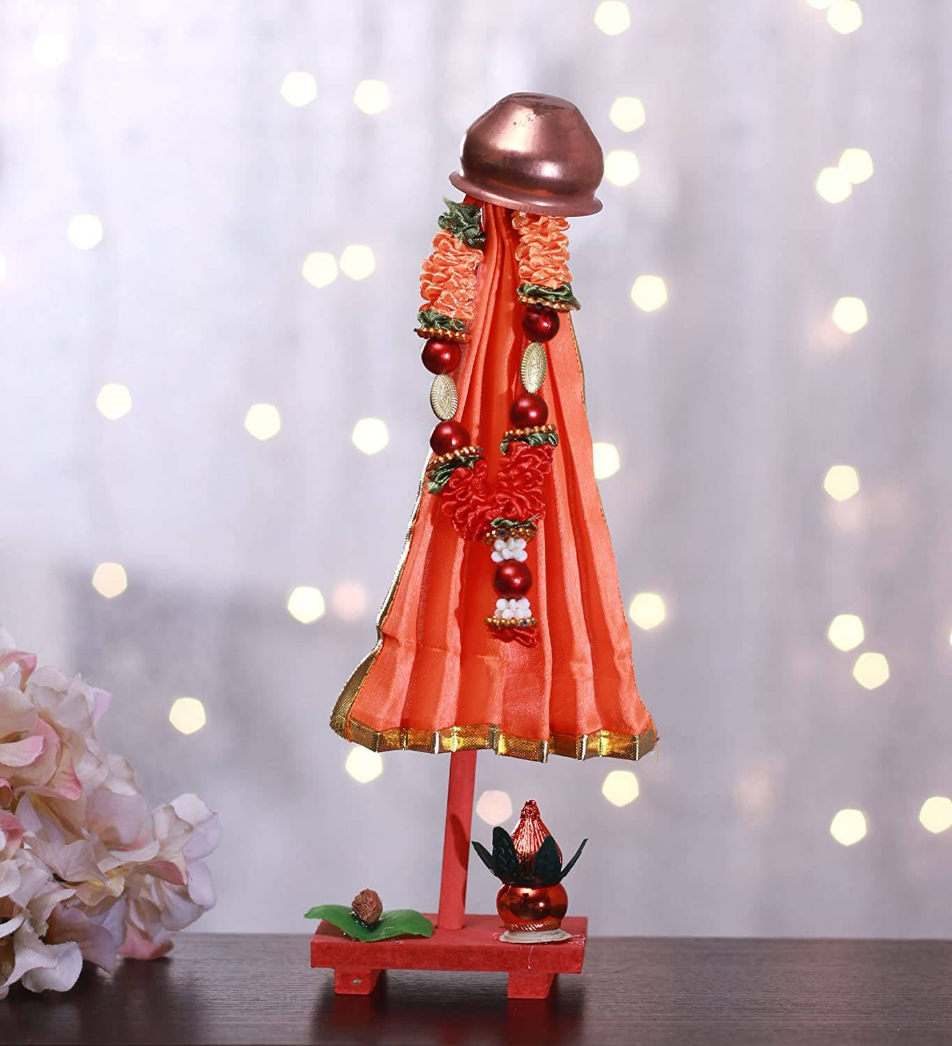 Gudi Padwa 桌布 壁紙 — 一個鮮紅色的裝飾性神像，飾有花環珠子和一個銅壺，立在一個紅色基座上，背景是柔和模糊的溫暖仙女燈光。