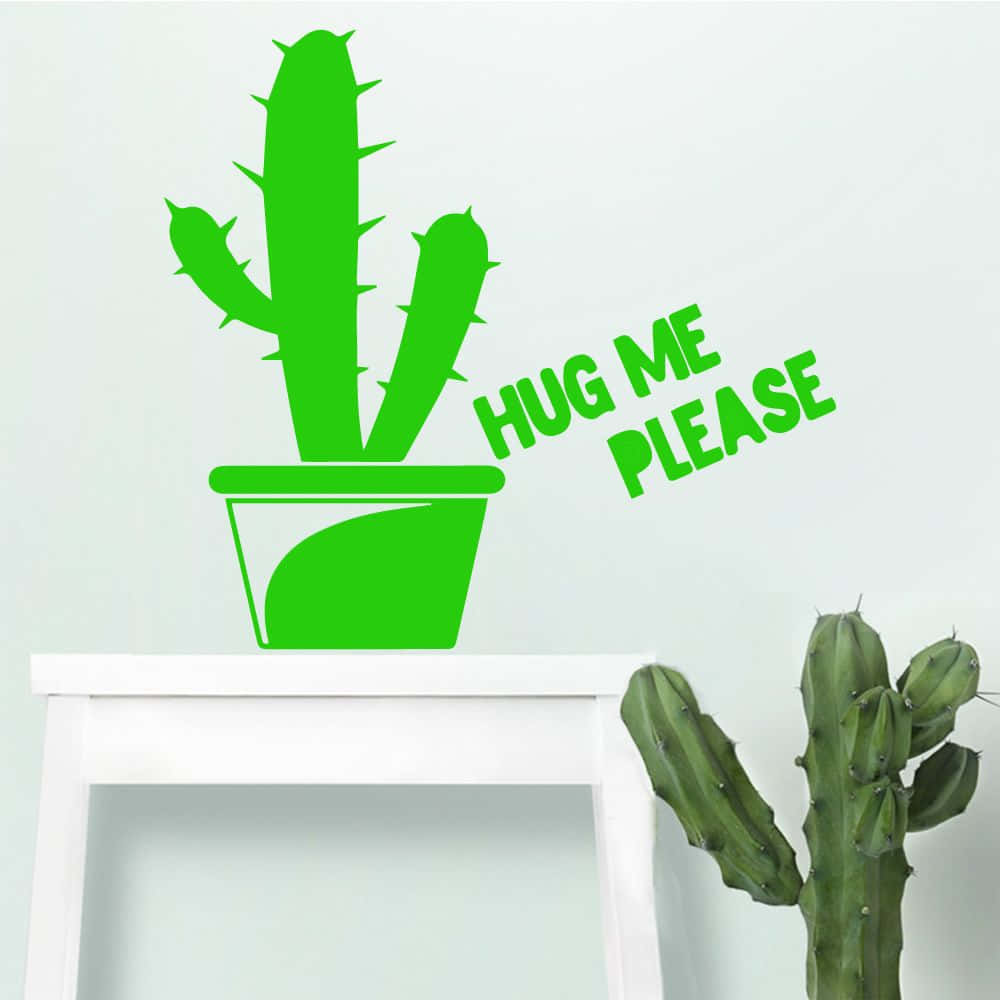 Kawaii Cactus 桌布 壁紙 — 一個鮮綠色仙人掌牆貼，上面有「HUG ME PLEASE」字樣，位於白色層架上的一個真實仙人掌上方，背景是素色牆壁。