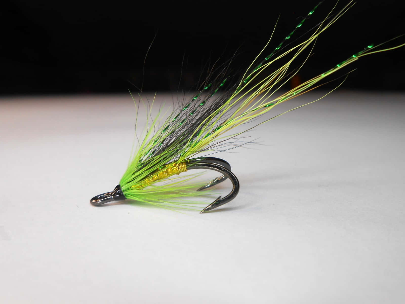 Fishing Bait 桌布 壁紙 — 一個鮮豔綠色和黑色的飛蠅釣魚假餌特寫，帶有閃爍纖維，背景為純白色。