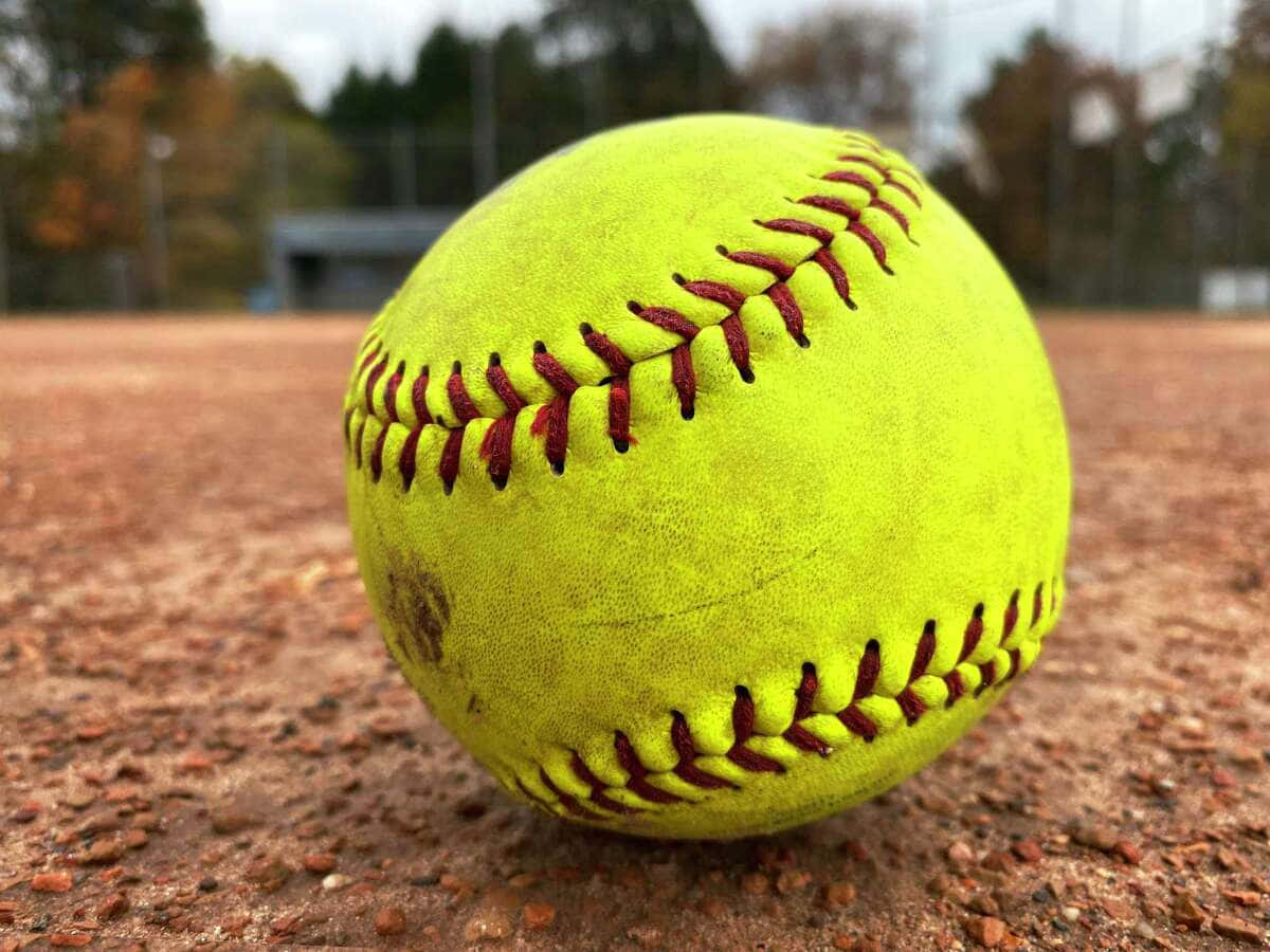Softball 桌布 壁紙 — 一個鮮黃色、帶紅色縫線的壘球特寫，放置在紅褐色泥土場地上。