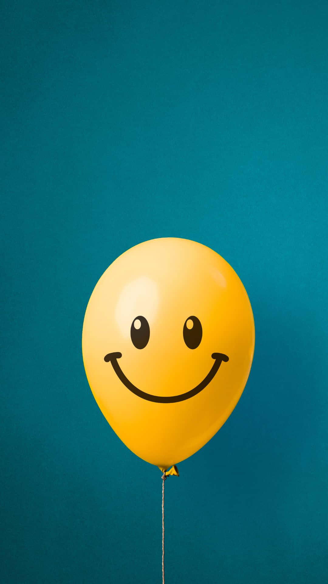 Happy iPhone 桌布 壁紙 — 一個鮮黃色氣球帶有簡單的黑色笑臉，漂浮在純青色背景上。