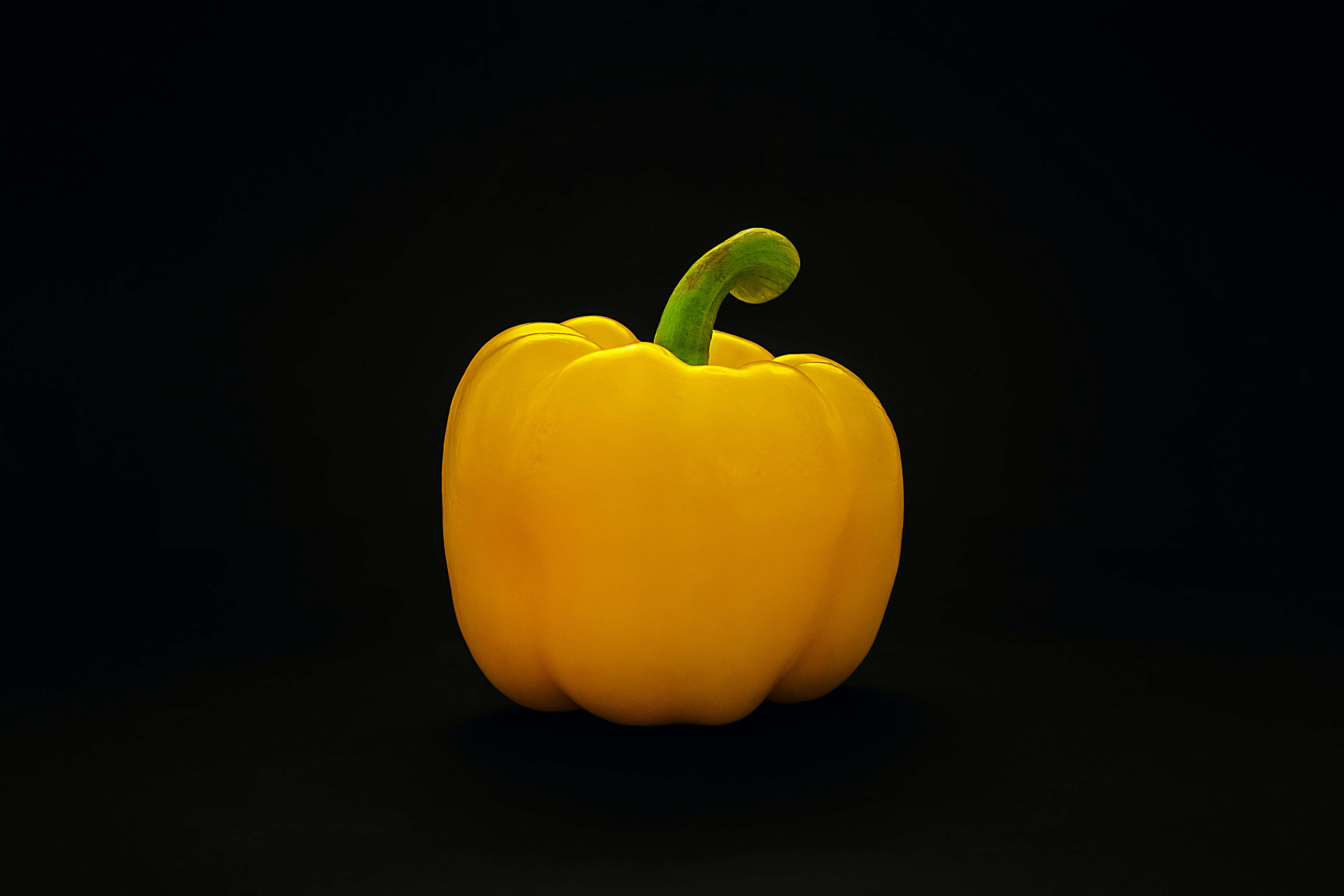 Yellow Bell Pepper 桌布 壁紙 — 一個鮮黃色的燈籠椒，帶有綠色莖部，孤立在深黑色背景前。