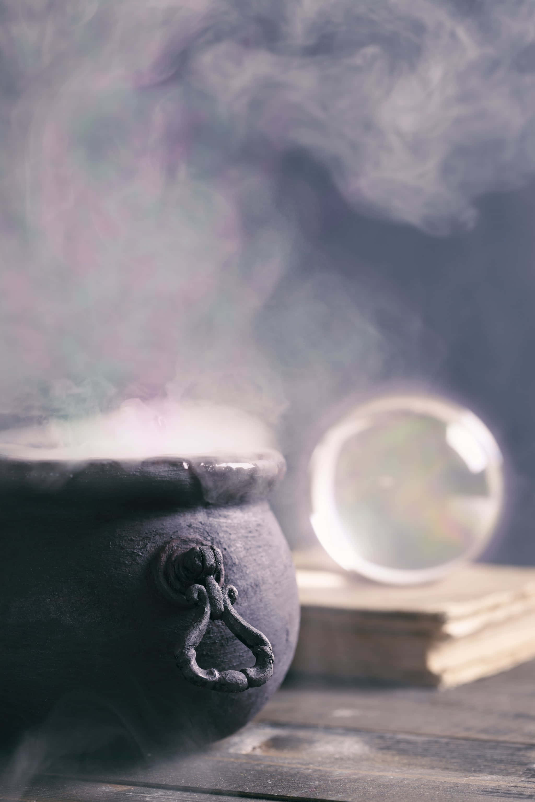 cauldron 桌布 壁紙 — 一個黑暗的大鍋神秘地冒著蒸氣，旁邊的水晶球放在木桌上舊書上。
