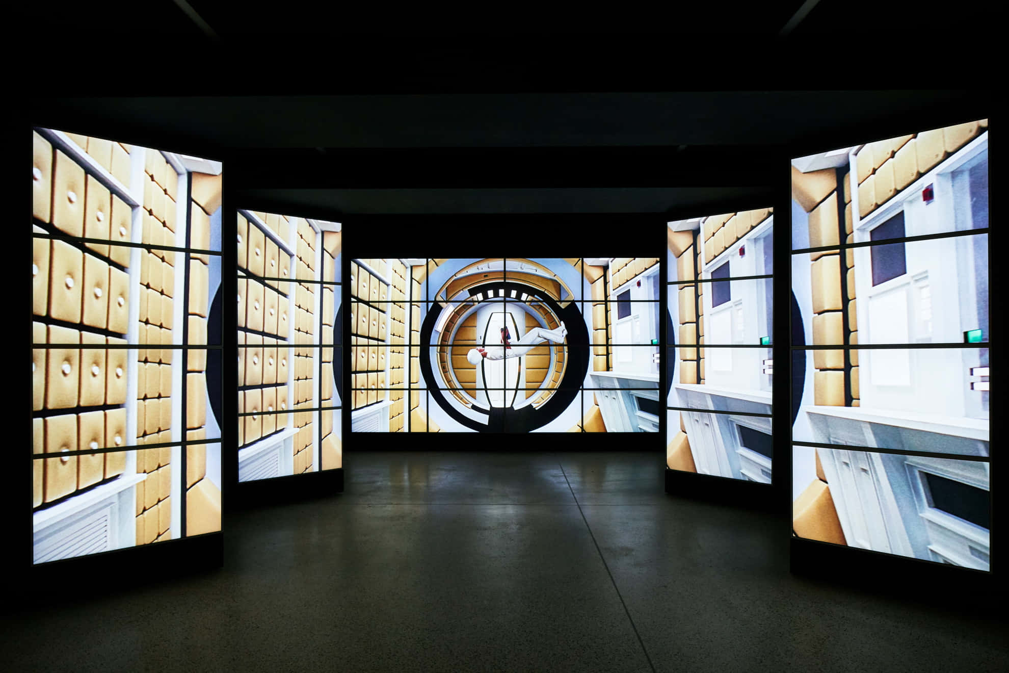 Exhibition 桌布 壁紙 — 一個黑暗的房間設有彎曲的數碼屏幕，顯示重複的黃色文件櫃和白色門的圖案，中央有一個圓形投影。