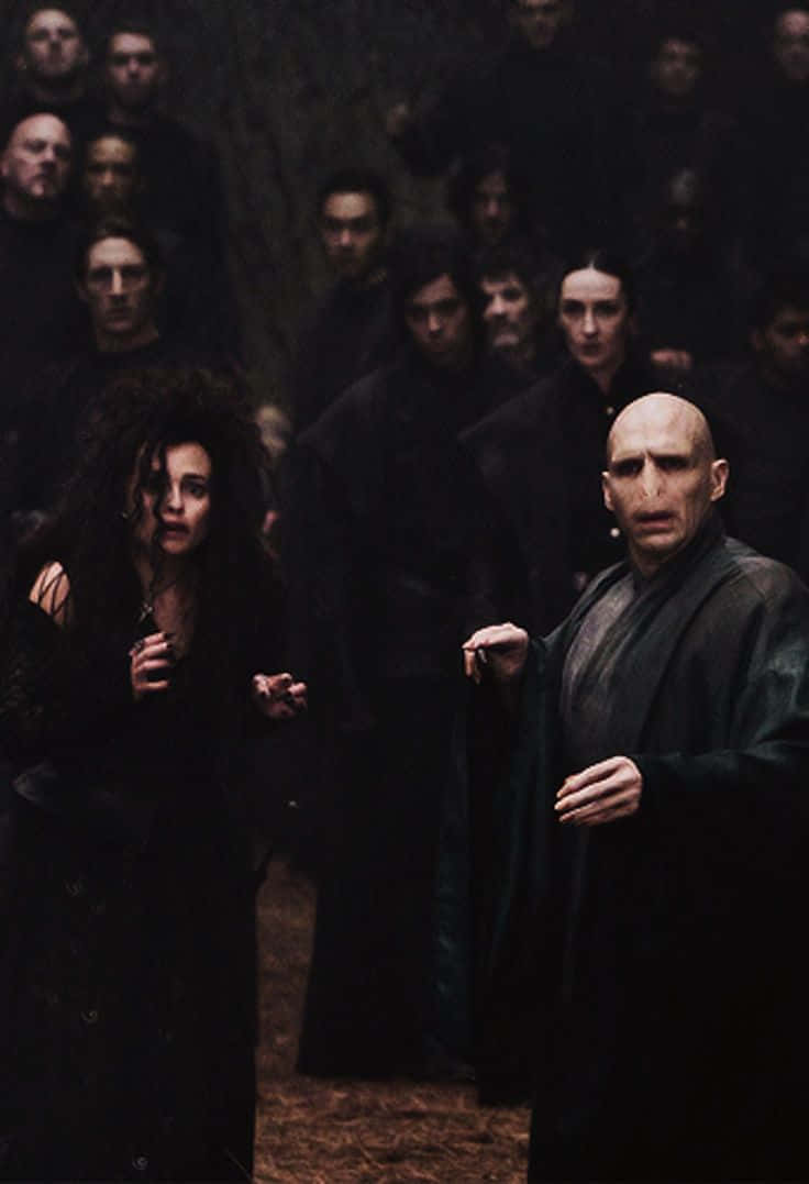 Death Eaters 桌布 壁紙 — 一個黑暗的電影場景，兩個身穿黑色長袍的中心人物被一群人在昏暗的森林中包圍。