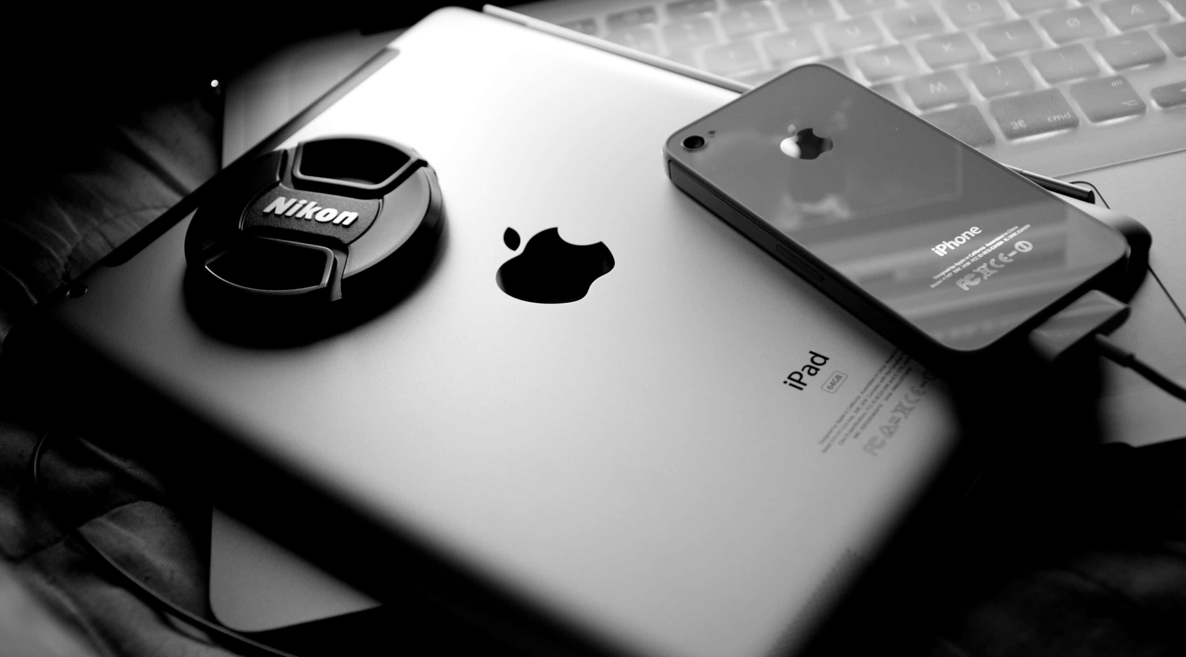 4K Apple 桌布 壁紙 — 一個黑白特寫，Nikon鏡頭蓋放在iPad上，旁邊有iPhone，下方是手提電腦鍵盤。