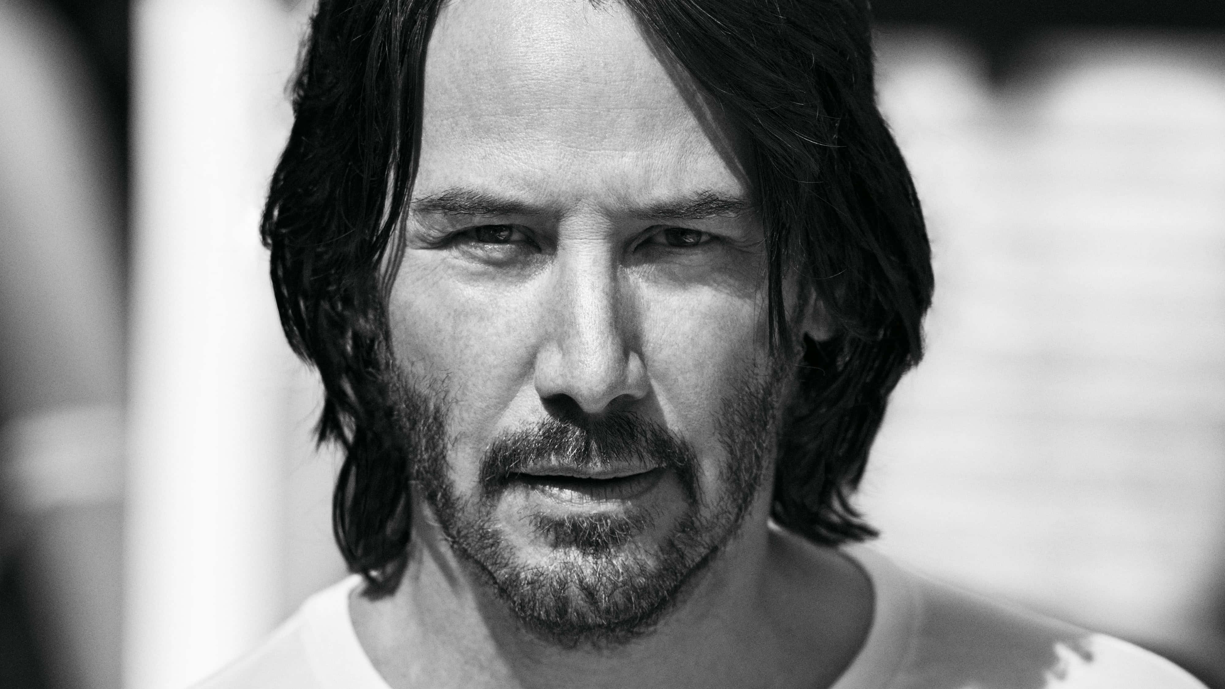 Keanu Reeves 桌布 壁紙 — 一個黑白特寫肖像，一名留著長黑髮和鬍鬚的男子，表情嚴肅地直視鏡頭。