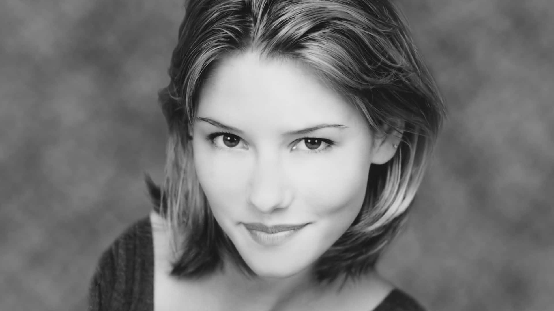 Chyler Leigh 桌布 壁紙 — 一個黑白肖像，一位留著及肩長髮的女性在紋理背景前對著鏡頭溫柔微笑。