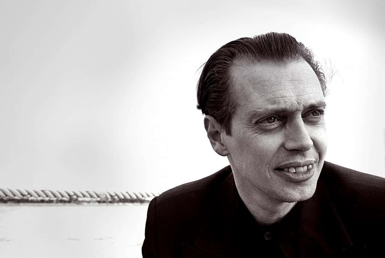 steve buscemi 桌布 壁紙 — 一個黑白肖像，一個向後梳頭髮的男人，在一個有繩索細節的簡單背景前微微微笑。