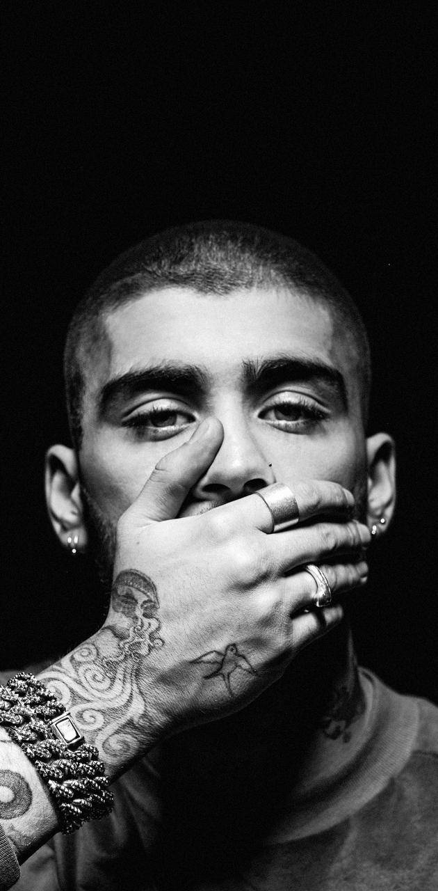 One Direction 桌布 壁紙 — 一個黑白肖像，一名男子手上和手腕佈滿紋身，在深色背景下用手指摀住嘴巴。