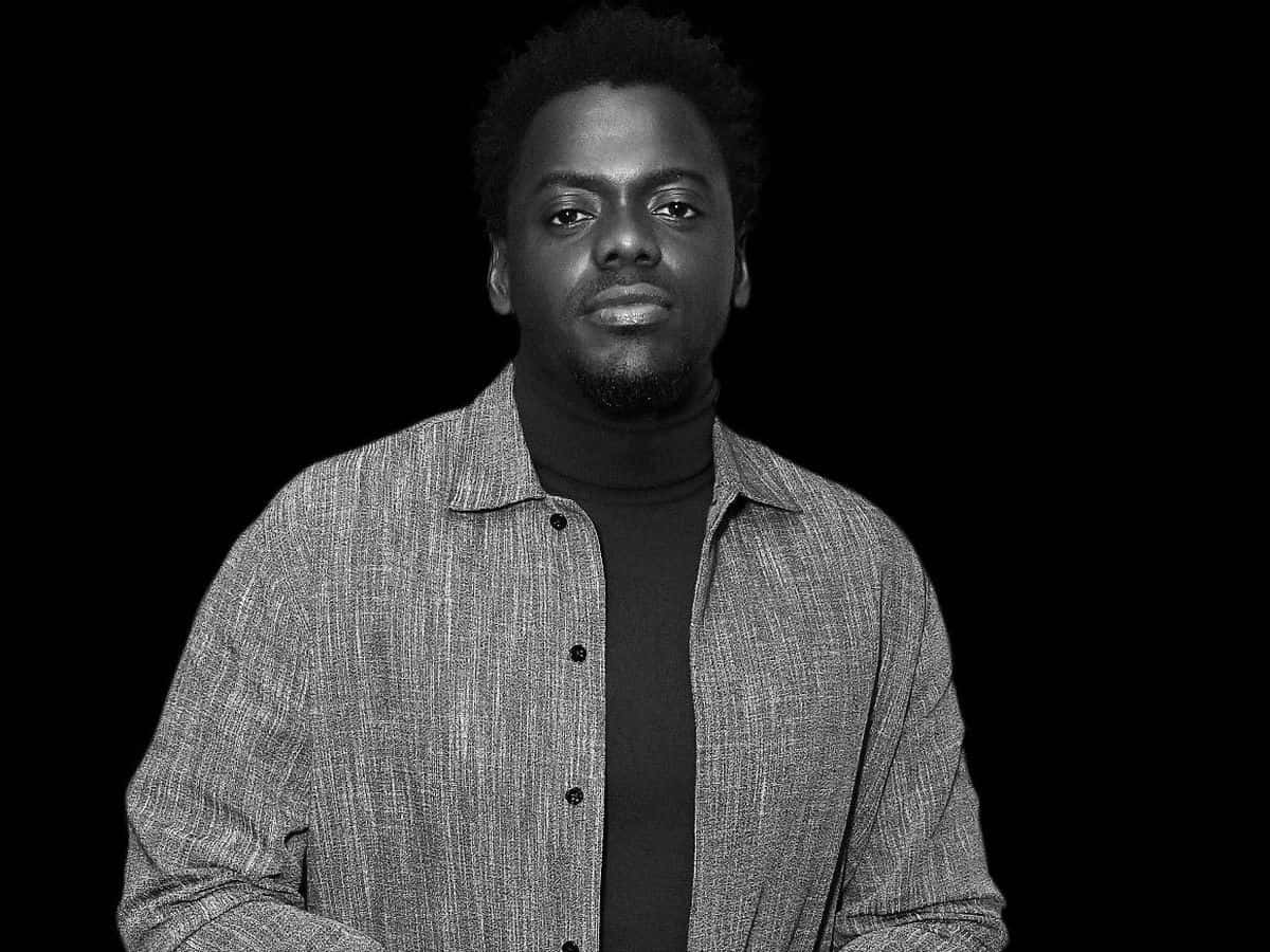 Daniel Kaluuya 桌布 壁紙 — 一個黑白肖像，一名表情嚴肅的男子穿著質感鈕扣襯衫內搭高領衫，背景為純黑色。