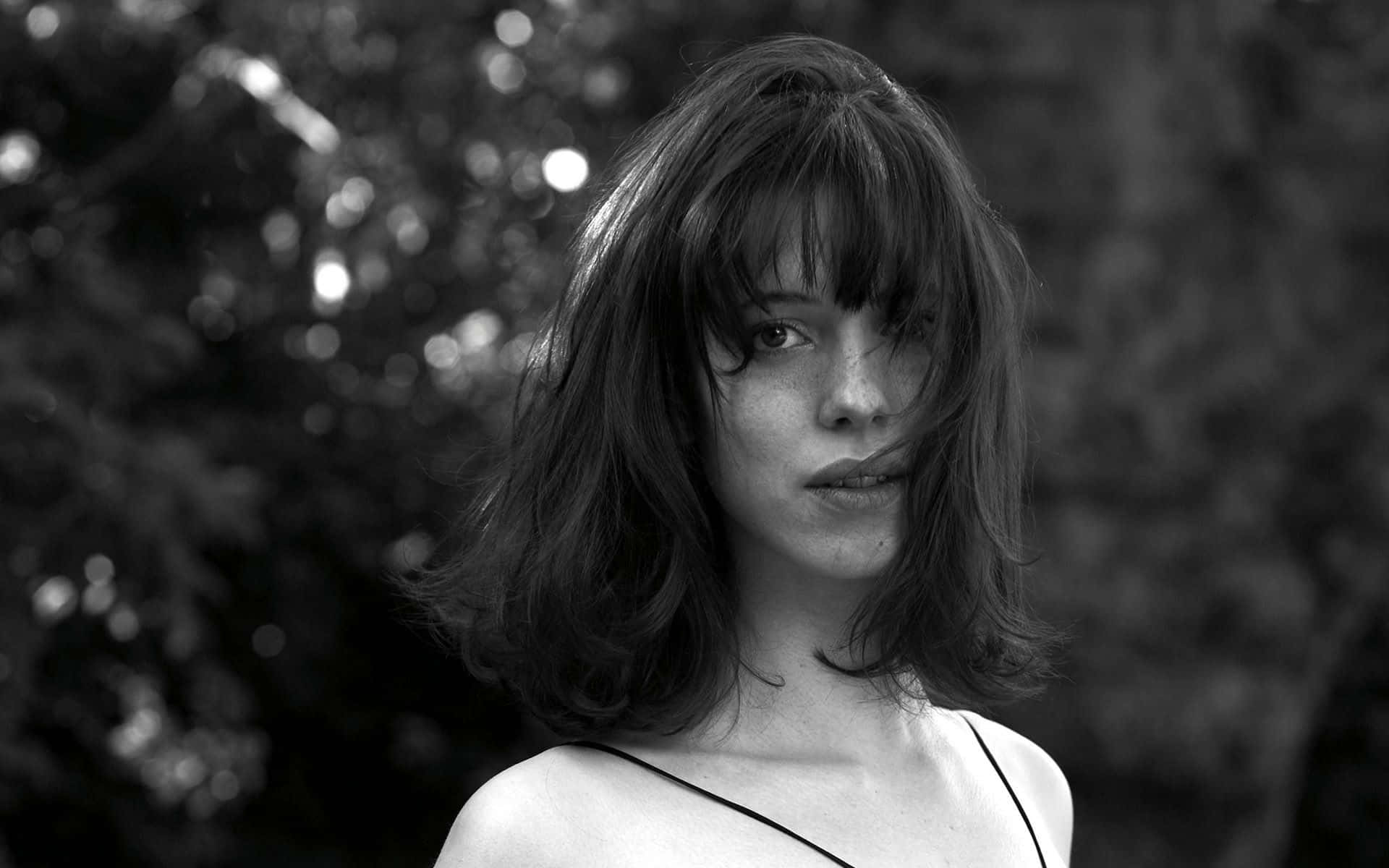 Rebecca Hall 桌布 壁紙 — 一個黑白肖像，一名頭髮蓬亂的女子在模糊的樹葉背景下直視鏡頭。