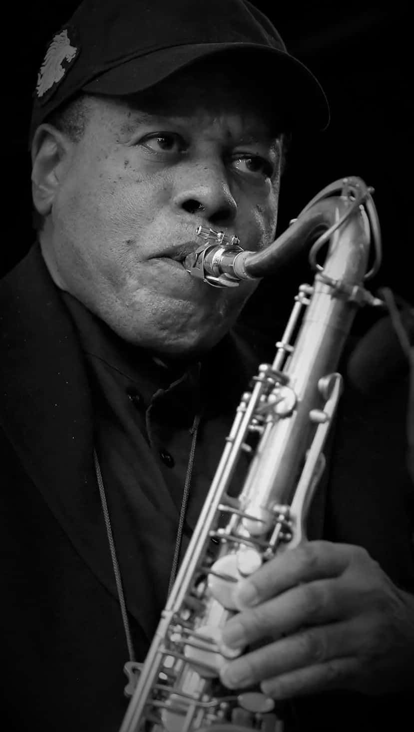 Wayne Shorter 桌布 壁紙 — 一個黑白肖像，捕捉一名男子專注地吹奏色士風的強烈神情。