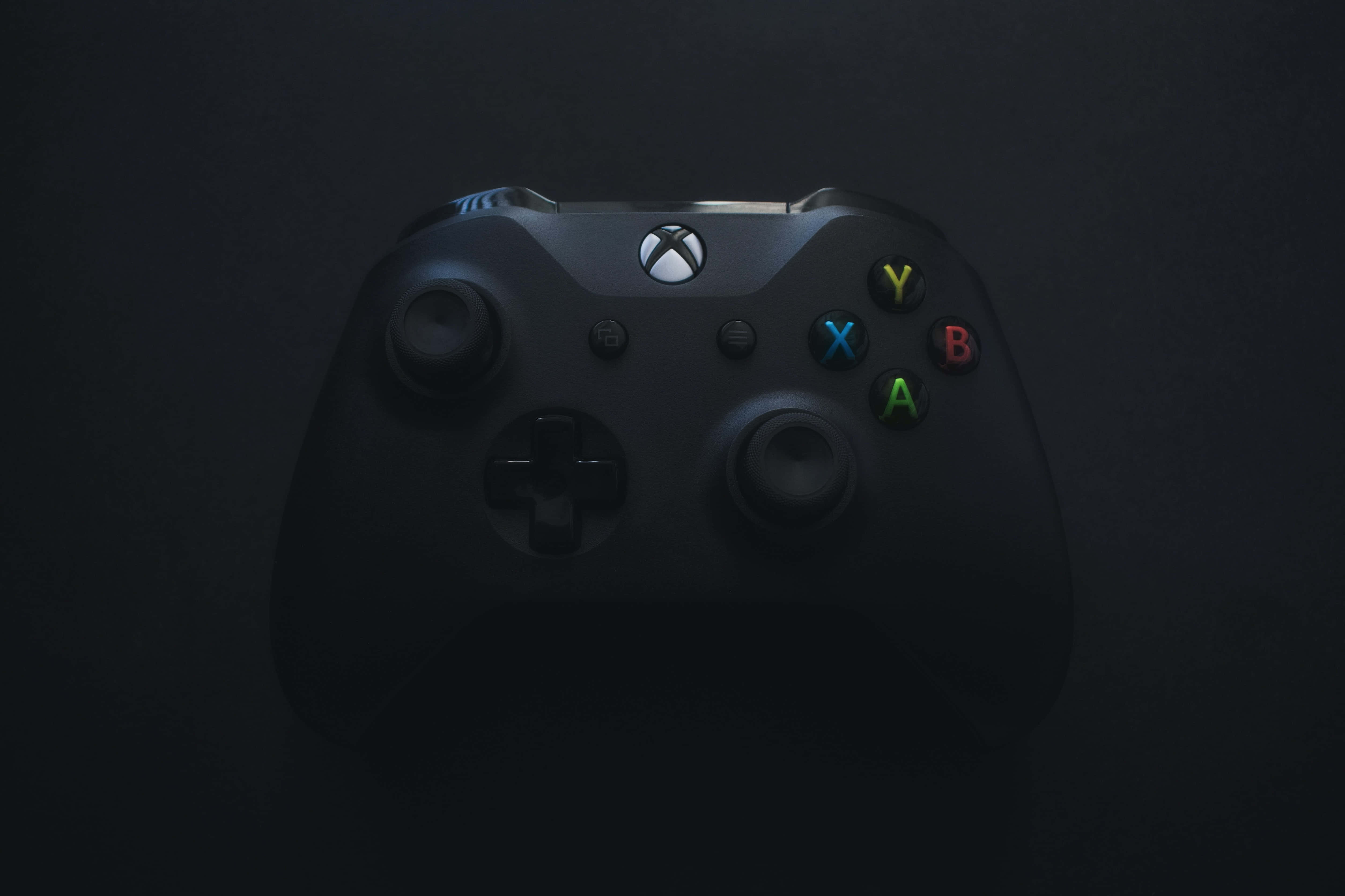 Gamer 桌布 壁紙 — 一個黑色Xbox手掣在深色背景上微微發光，彩色按鈕被照亮。