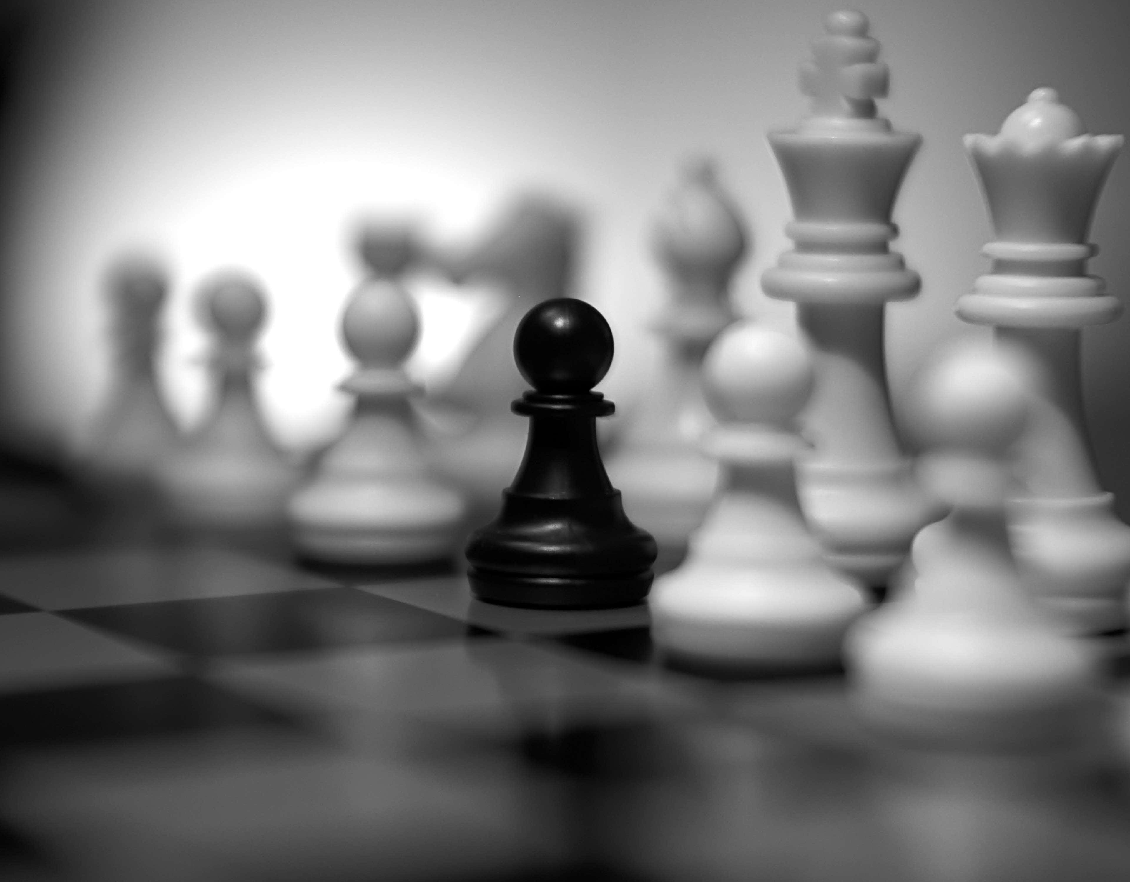 Black And White Chess 桌布 壁紙 — 一個黑色國際象棋兵在棋盤上清晰對焦，周圍是模糊的白色棋子，呈單色。