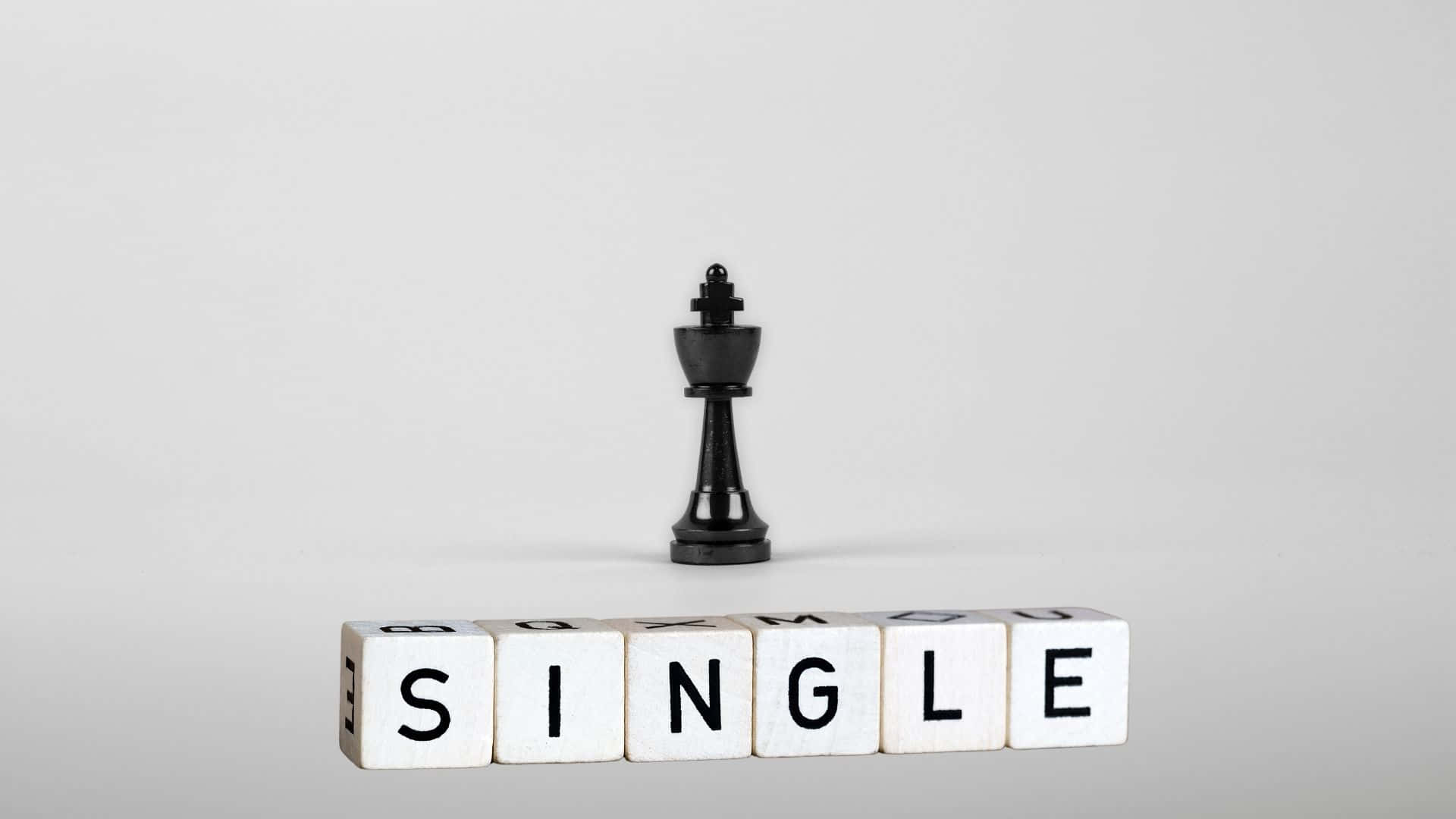 Single 桌布 壁紙 — 一個黑色國際象棋國王獨自站立在由白色木塊拼成的「SINGLE」一詞上方，背景為純灰色。