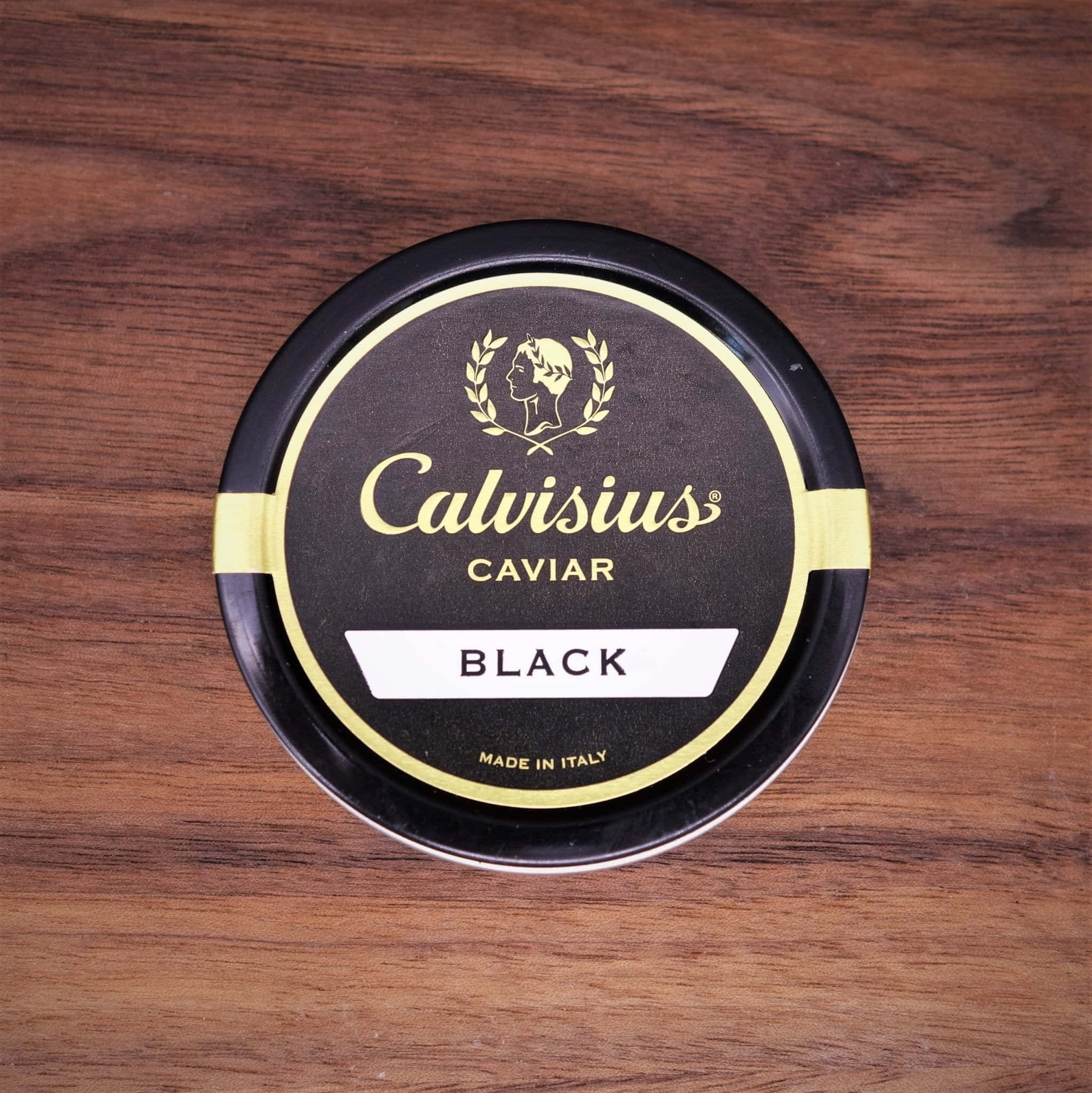 Black Caviar 桌布 壁紙 — 一個黑色圓形嘅Calvisius Caviar Black鞋油罐擺喺一塊豐富嘅棕色木質表面上。