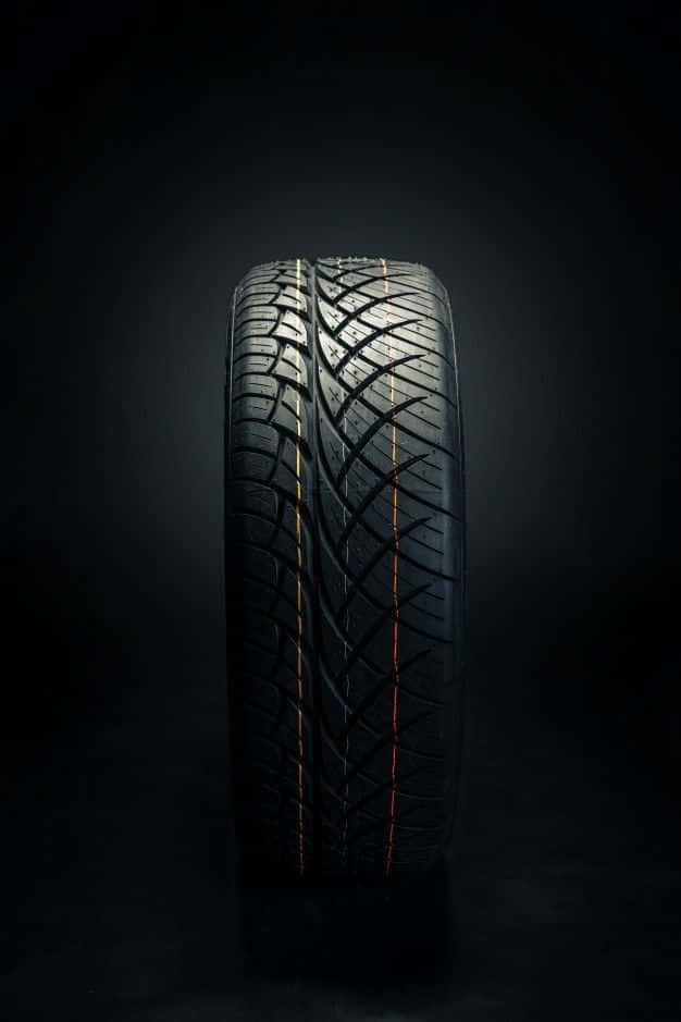 Winter Tires 桌布 壁紙 — 一個黑色汽車輪胎直立於深色背景前，戲劇性的燈光突顯其胎面花紋和橙色裝飾條。
