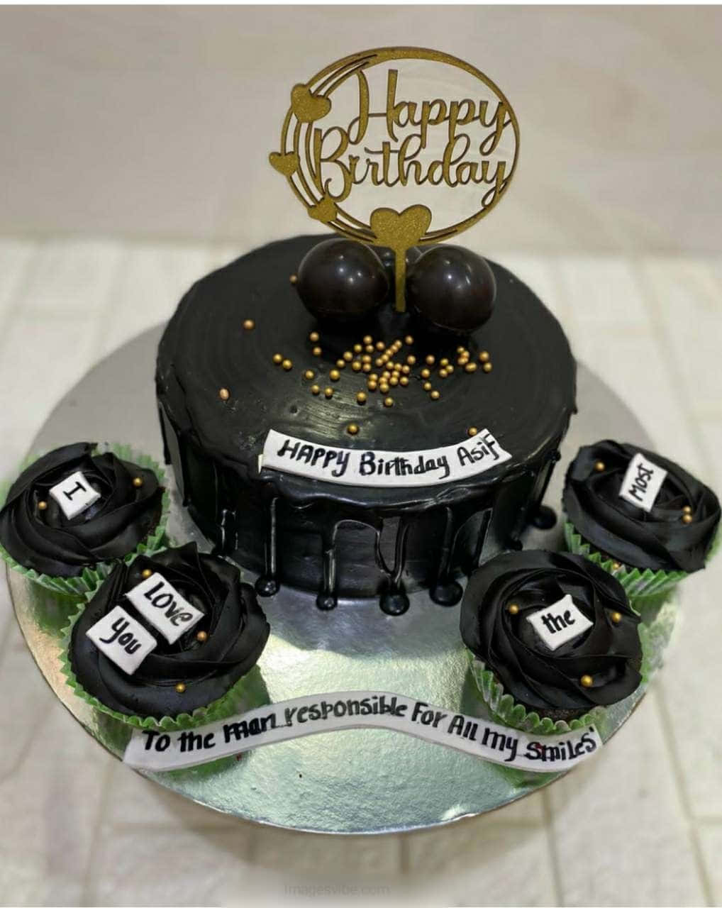 生日蛋糕 桌布 壁紙 — 一個黑色滴落蛋糕，上面有金色糖粒和「Happy Birthday」裝飾，周圍環繞著拼出「I love you the most」的杯子蛋糕，放在銀盤上。