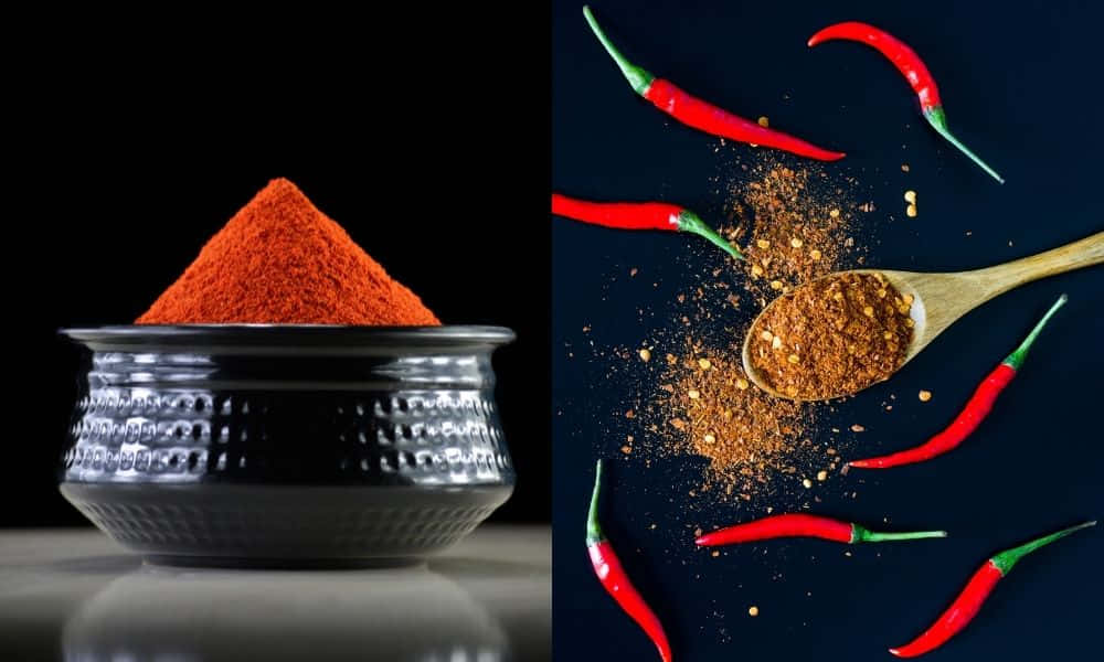 Red Chili Powder 桌布 壁紙 — 一個黑色碗盛著一團鮮豔的橙紅色辣椒粉，旁邊有散落的完整紅辣椒和一把帶有研磨香料的木勺，背景為深色。