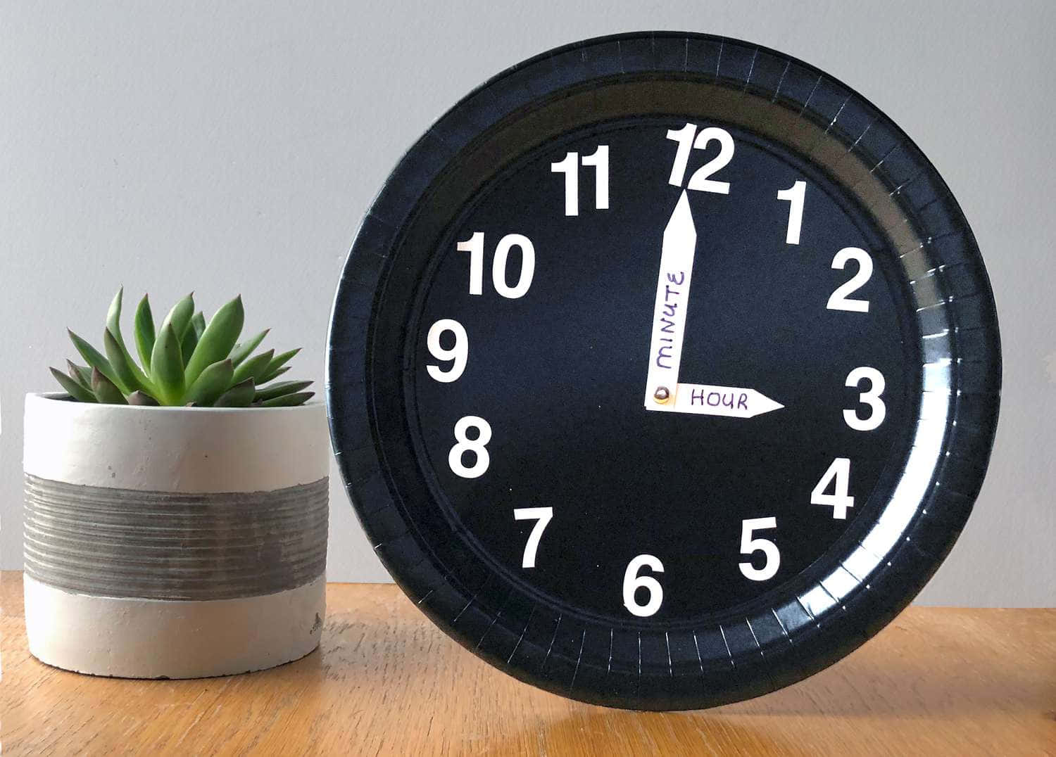 Clocks 桌布 壁紙 — 一個黑色紙碟時鐘，帶有白色數字和指針，放在木桌上的一盆多肉植物旁邊。