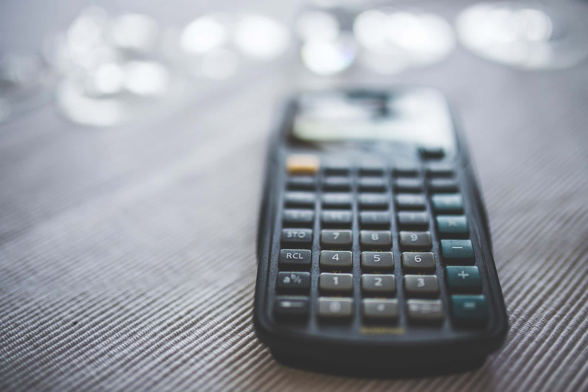 Calculator 桌布 壁紙 — 一個黑色計算機放在有紋理的灰色表面上，背景有柔和散景燈光。