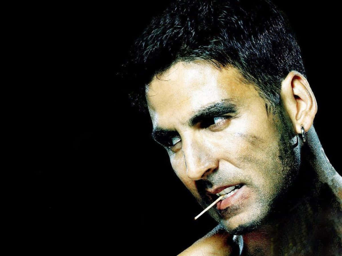 Akshay Kumar 桌布 壁紙 — 一個黑髮戴耳環的男人在黑色背景和戲劇性燈光下吸煙。