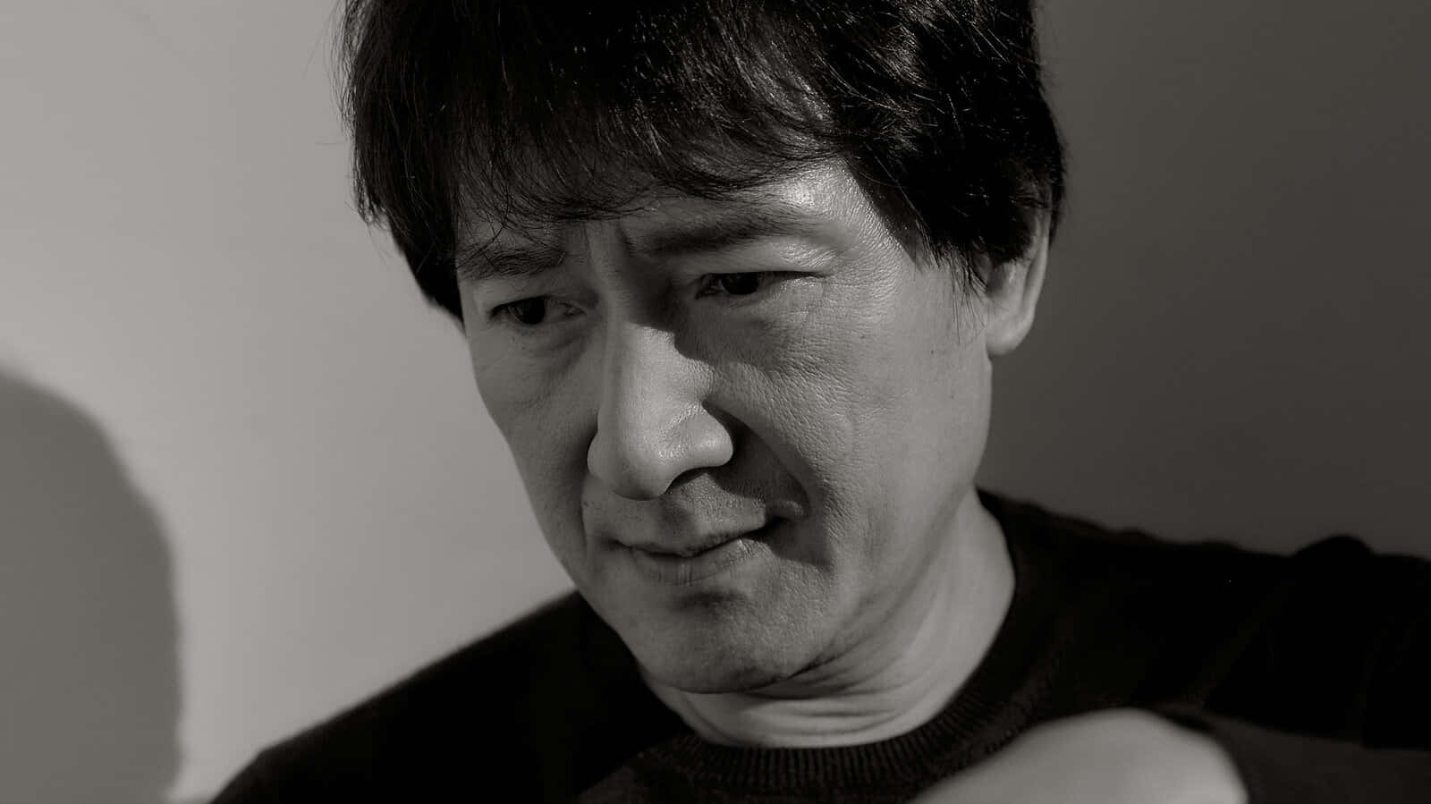 Ke Huy Quan 桌布 壁紙 — 一個黑髮男人低頭沉思的黑白近距離肖像。