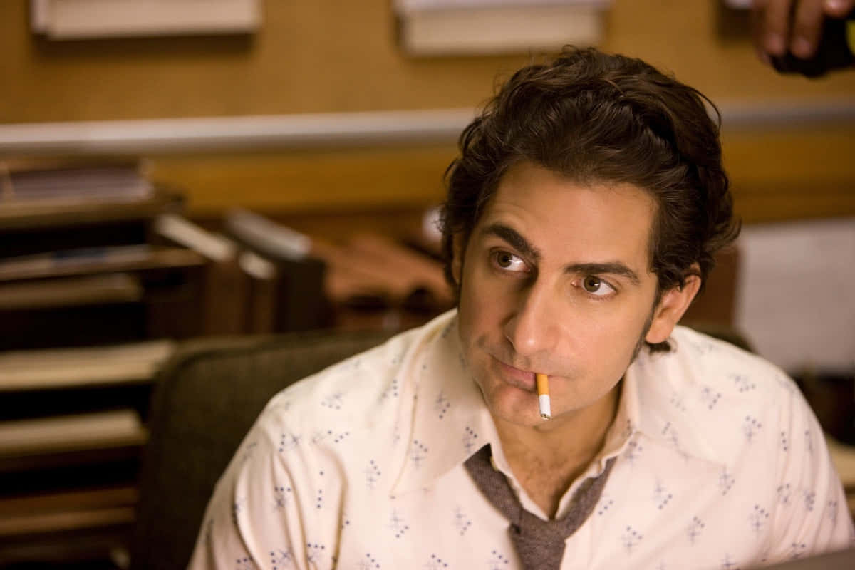 Michael Imperioli 桌布 壁紙 — 一個黑髮男人坐在辦公椅上，嘴裡叼著煙，視線望向一旁。