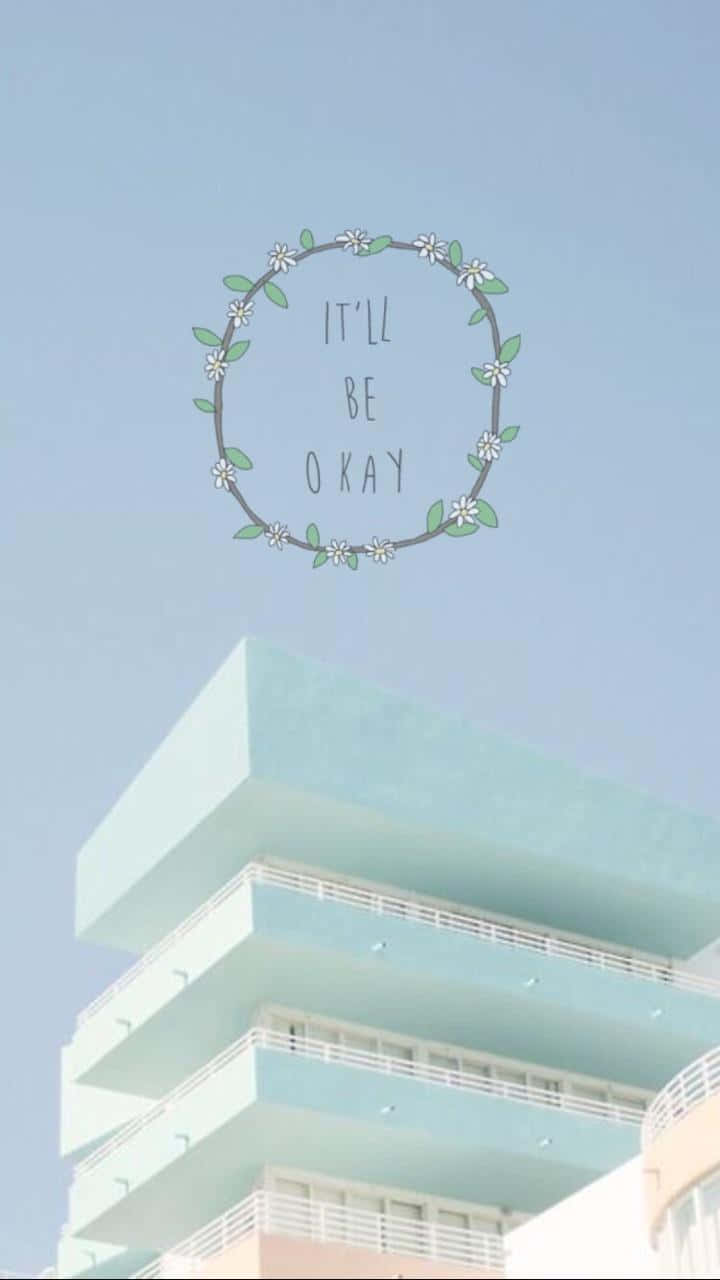 粉藍色建築物，帶有寫著「It'll be okay」的花環圖案，背景是晴朗天空。