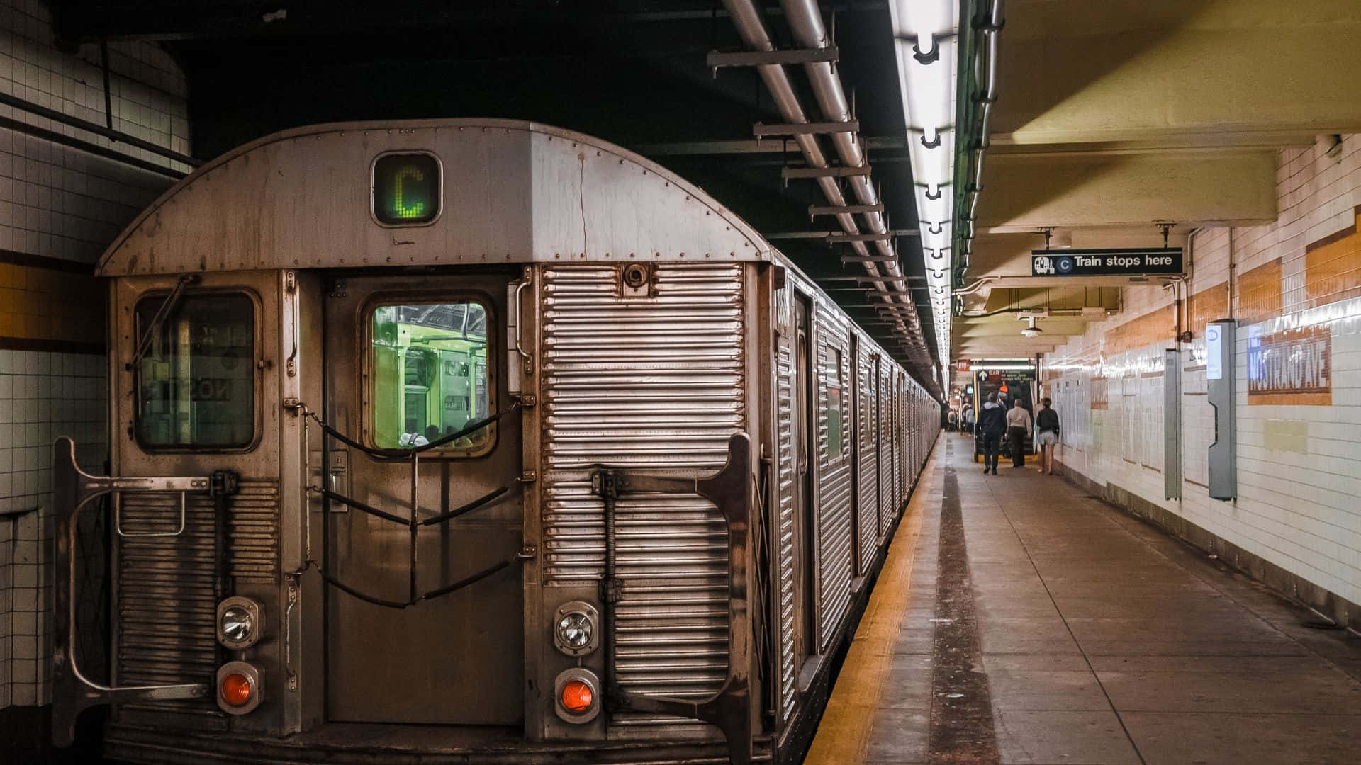 Subway 桌布 壁紙 — 一列復古地鐵列車帶有發光的綠色C標誌，停靠在瓷磚站台上，通勤者在螢光燈下走過。
