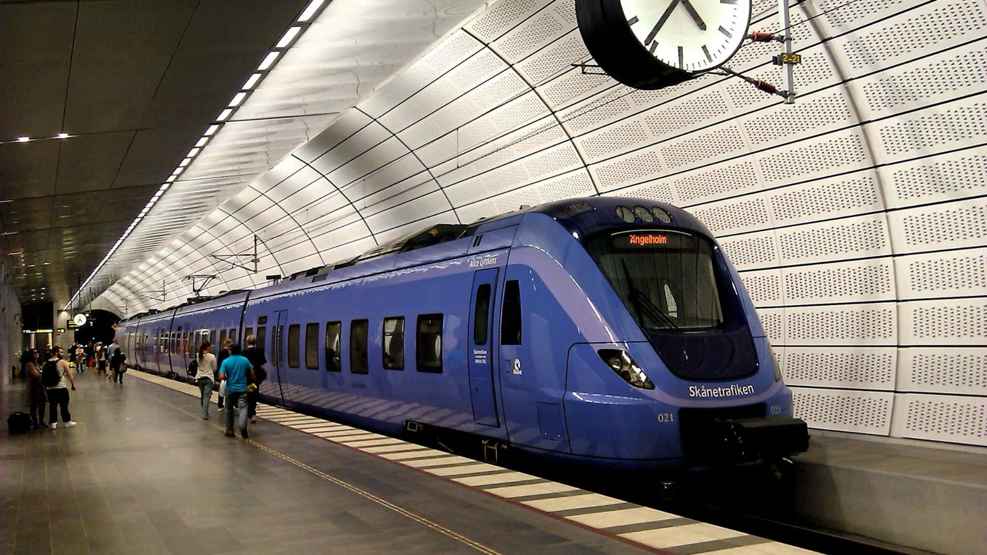 Subway 桌布 壁紙 — 一列時尚的藍色列車抵達現代化的地下車站，乘客在明亮的螢光燈下於月台等候。
