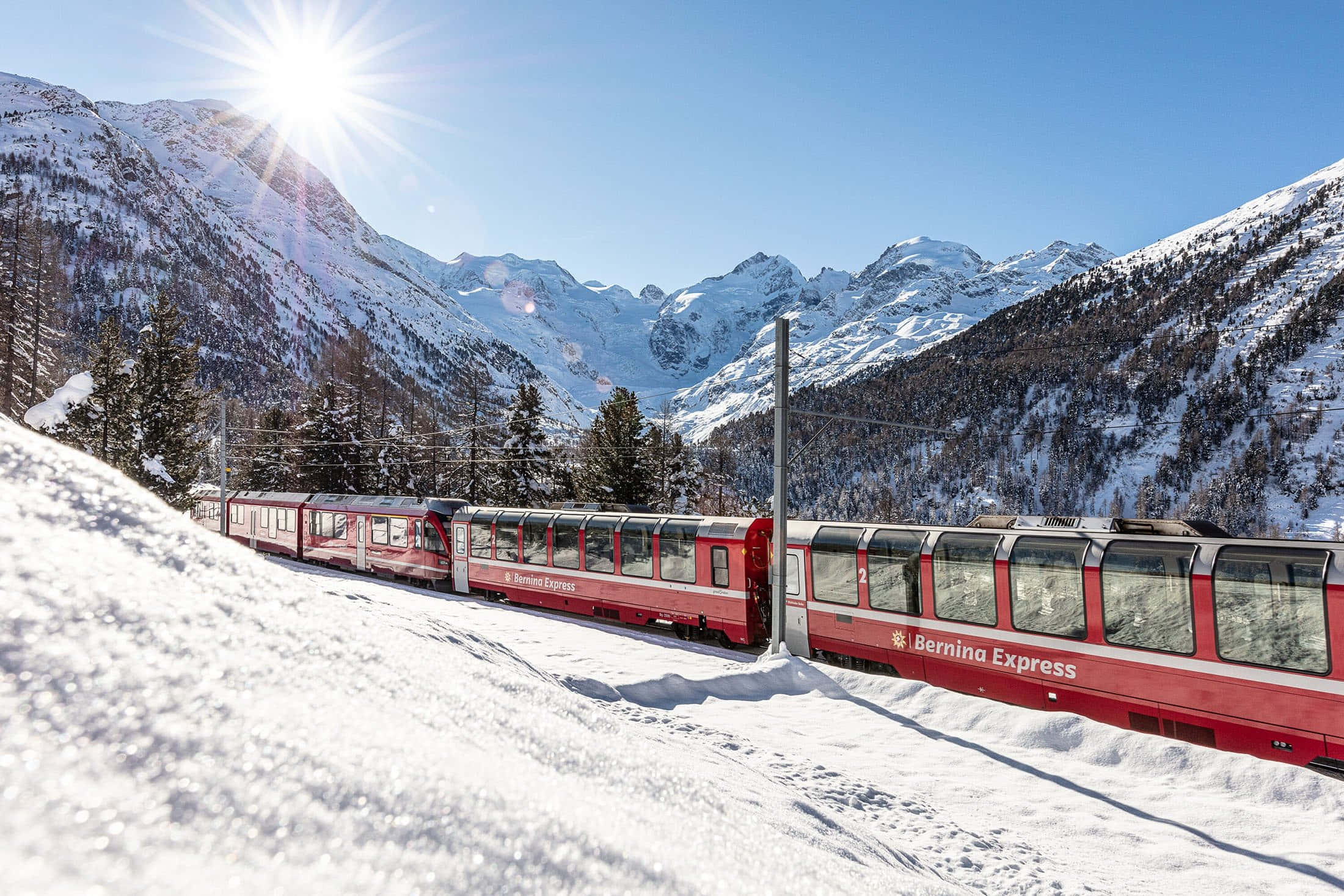 Switzerland 桌布 壁紙 — 一列紅色的伯爾尼納快車在明亮的陽光下蜿蜒穿過白雪覆蓋的阿爾卑斯山脈。