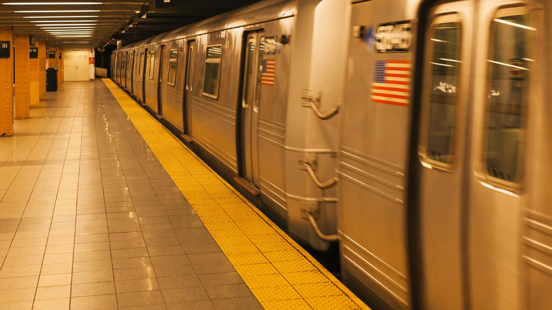 Subway 桌布 壁紙 — 一列銀色地鐵在溫暖的人造燈光下，駛過一條以鮮黃色安全線標記的瓷磚月台。