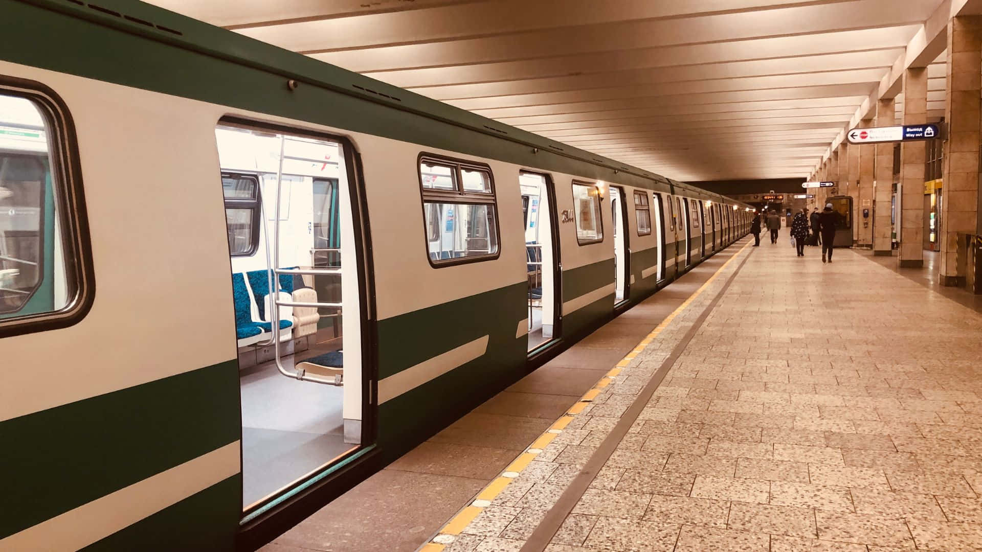 Subway 桌布 壁紙 — 一列長長的綠色和白色火車停在舖有瓷磚的地鐵月台上，遠處有乘客在溫暖的人造燈光下行走。