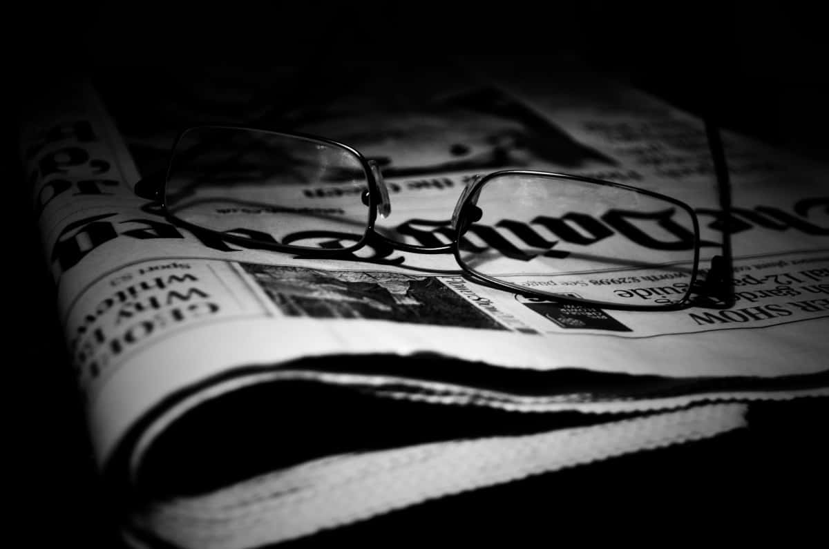Black And White Newspaper 桌布 壁紙 — 一副眼鏡放在摺疊的報紙上，以高對比度黑白照片呈現，帶有戲劇性的陰影。
