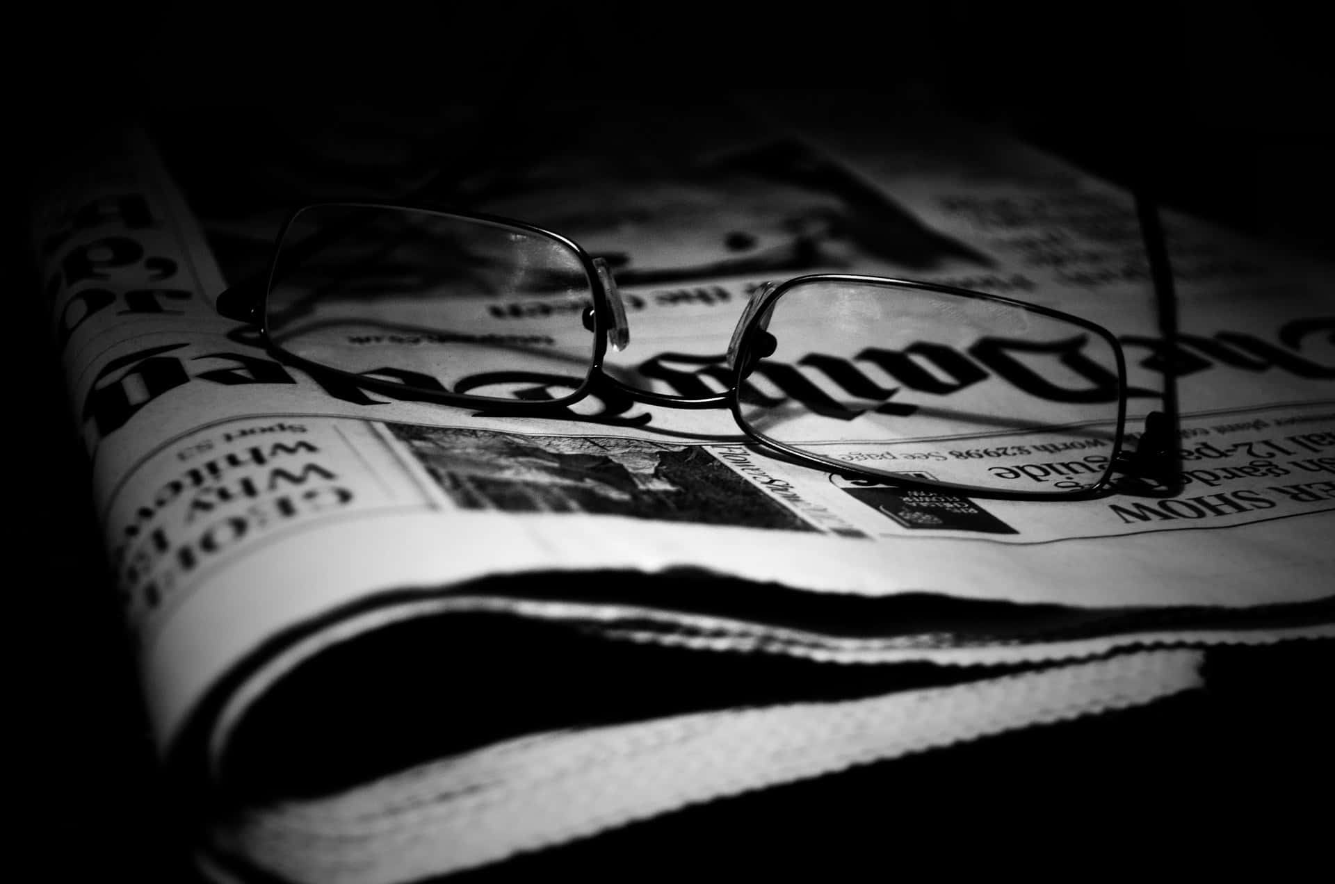 Journalism 桌布 壁紙 — 一副眼鏡放在摺疊的報紙上，呈現高對比度的黑白效果，帶有戲劇性的陰影。