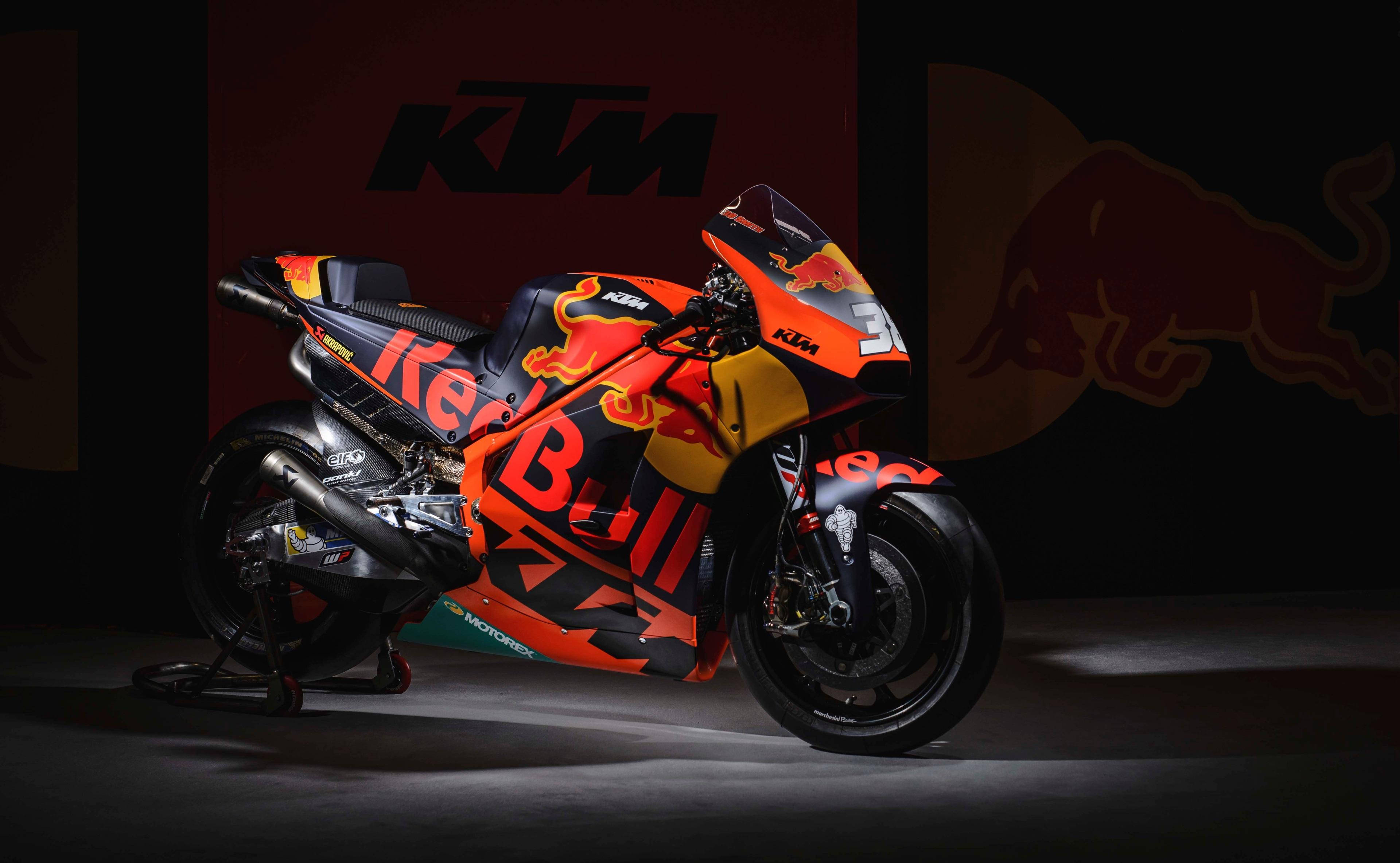 機車 桌布 壁紙 — 一台時尚的KTM Red Bull賽車摩托車，帶有鮮豔的橙色和黑色塗裝，在黑暗的攝影棚中對著品牌背景戲劇性地照明。