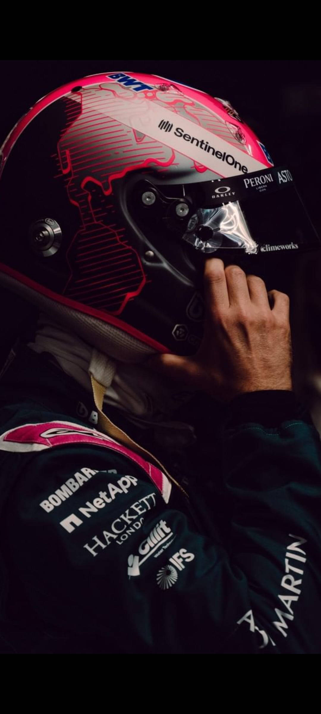sebastian vettel 桌布 壁紙 — 一名一級方程式車手在戲劇性燈光下調整他帶有贊助商標誌的粉紅色和黑色頭盔。
