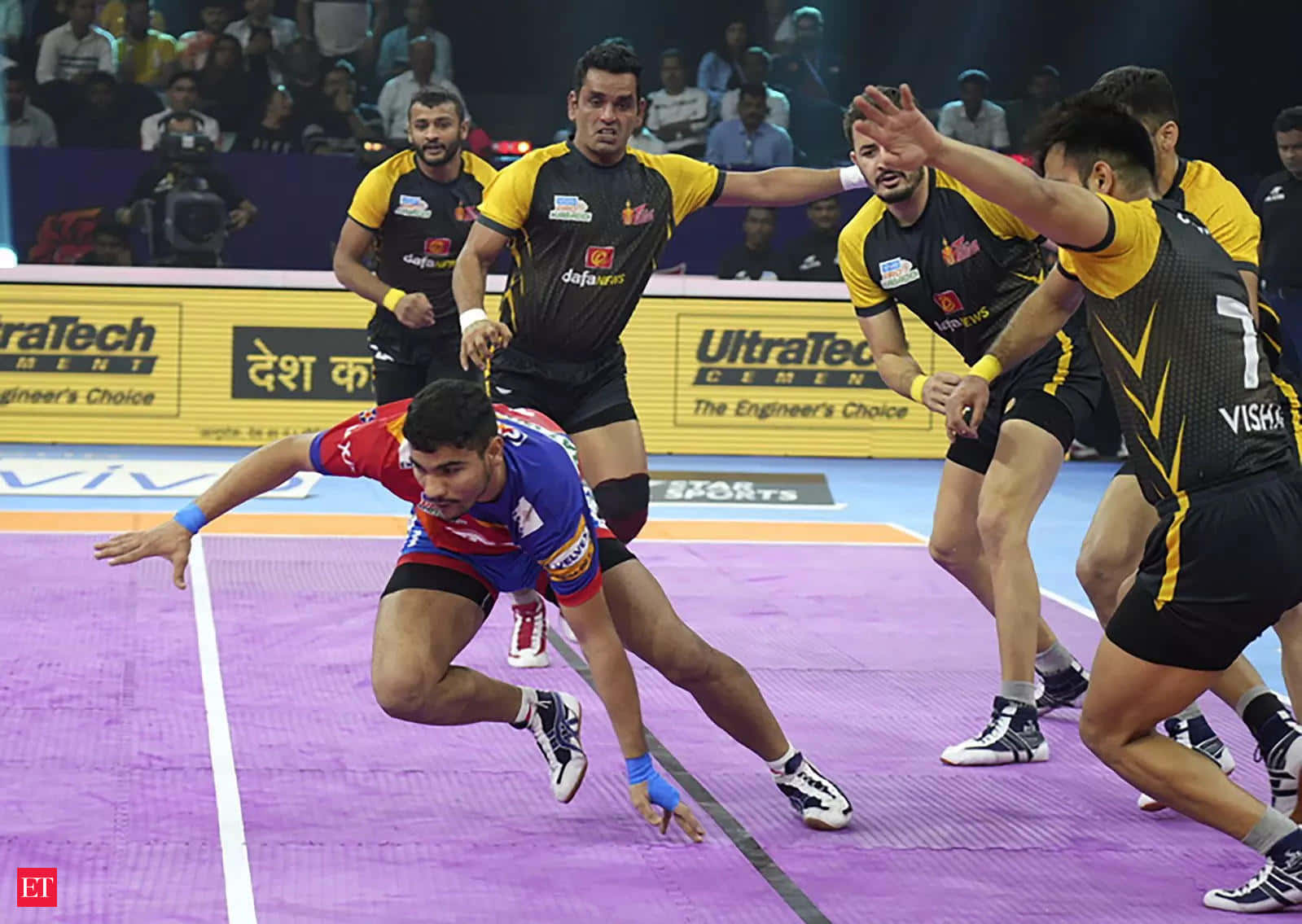 Kabaddi 桌布 壁紙 — 一名充滿活力的卡巴迪球員身穿紅藍色球衣，在紫色場地上低身潛入，而身穿黑黃色球衣的對手則跳起試圖攔截他。