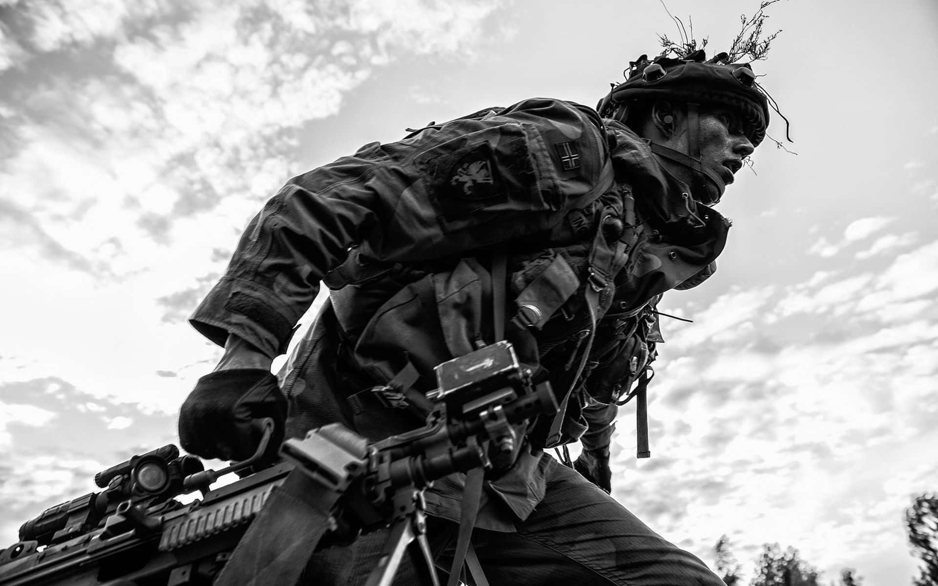 Army 桌布 壁紙 — 一名全副武裝的士兵在陰天背景下持步槍前進，呈現粗糙的黑白照片效果。