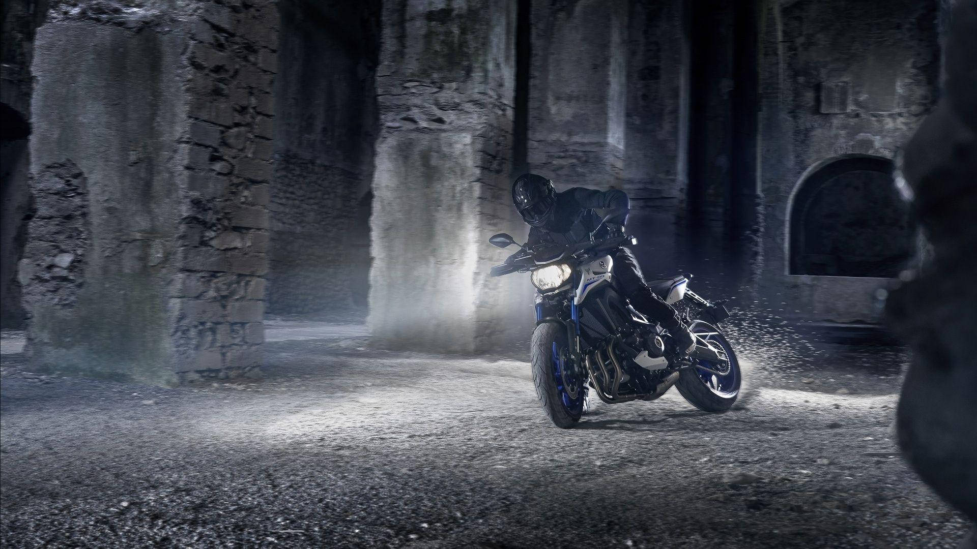 yamaha mt 15 桌布 壁紙 — 一名全副裝備的電單車手在夜間騎著堅固的電單車，穿過霧氣籠罩的古老石廢墟，傾身入彎。