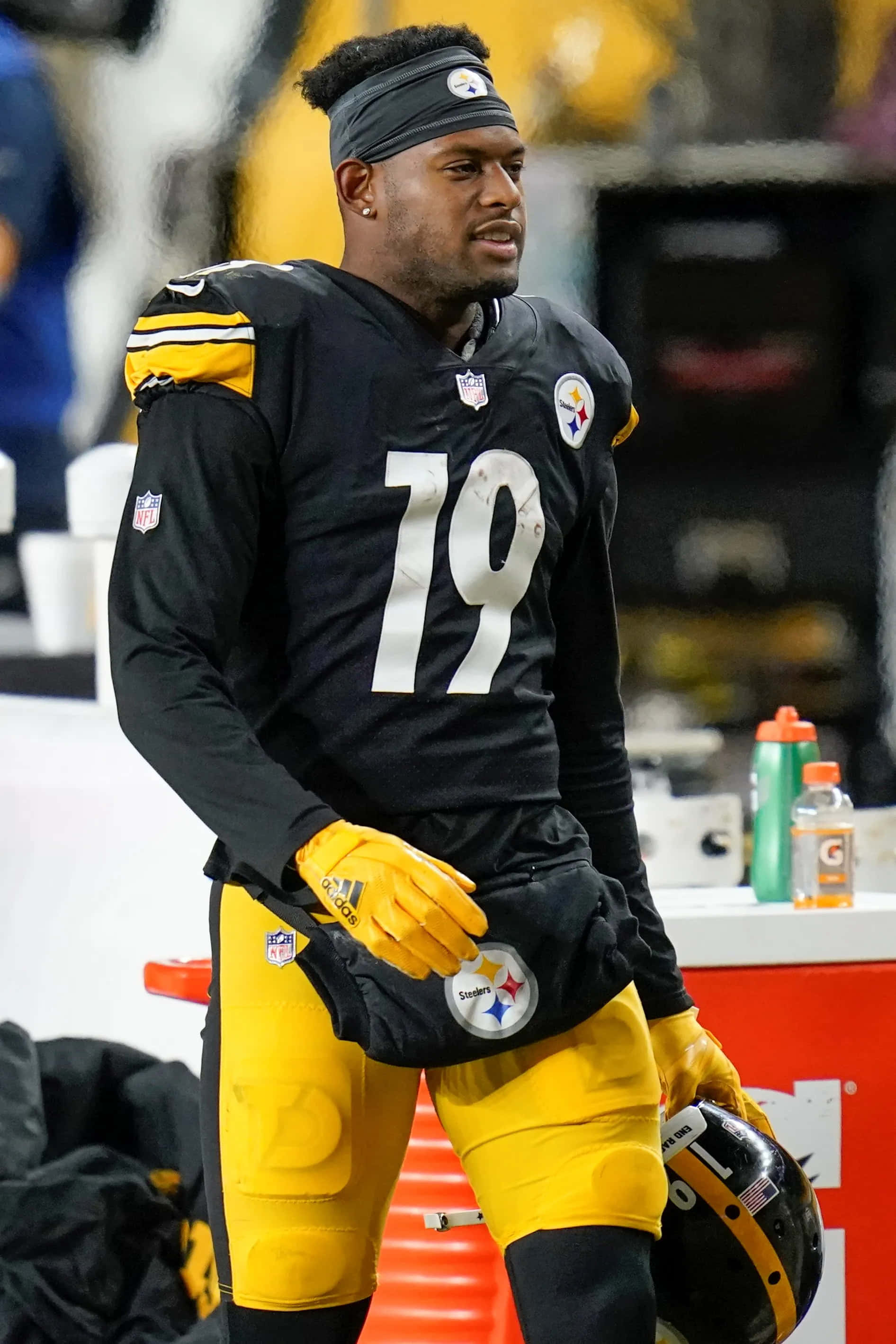 Juju Smith Schuster 桌布 壁紙 — 一名匹茲堡鋼人隊美式足球員身穿黑金色球衣，站在邊線手持頭盔。