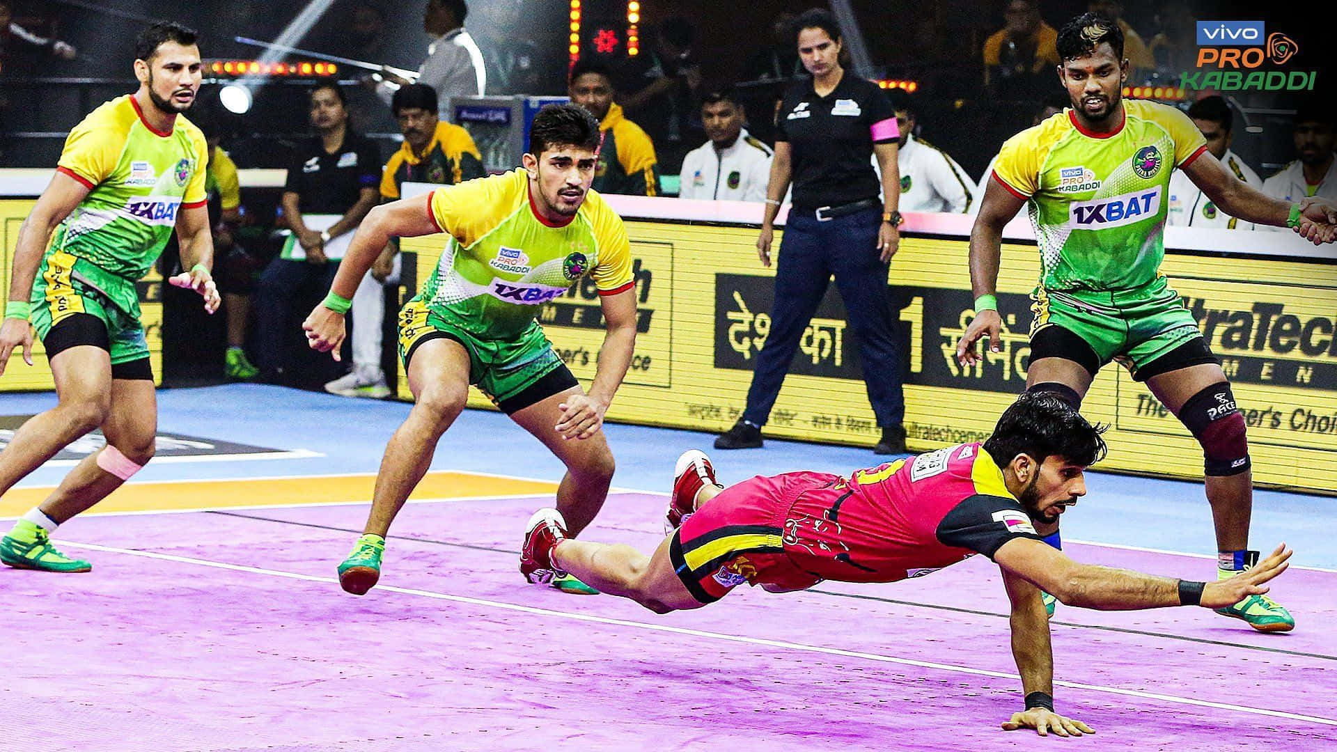Kabaddi 桌布 壁紙 — 一名卡巴迪球員在紫色場地上飛身撲出，身穿綠色和黃色球衣的對手在激烈的比賽中追趕他。