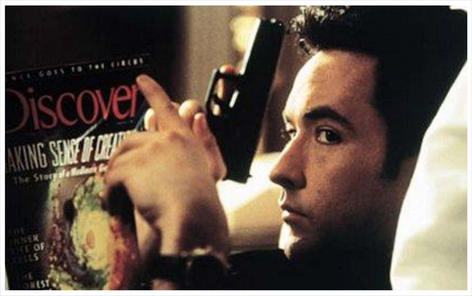 John Cusack 桌布 壁紙 — 一名在床上嘅男人喺溫暖燈光下，專注地將槍指向一本《Discover》雜誌封面。