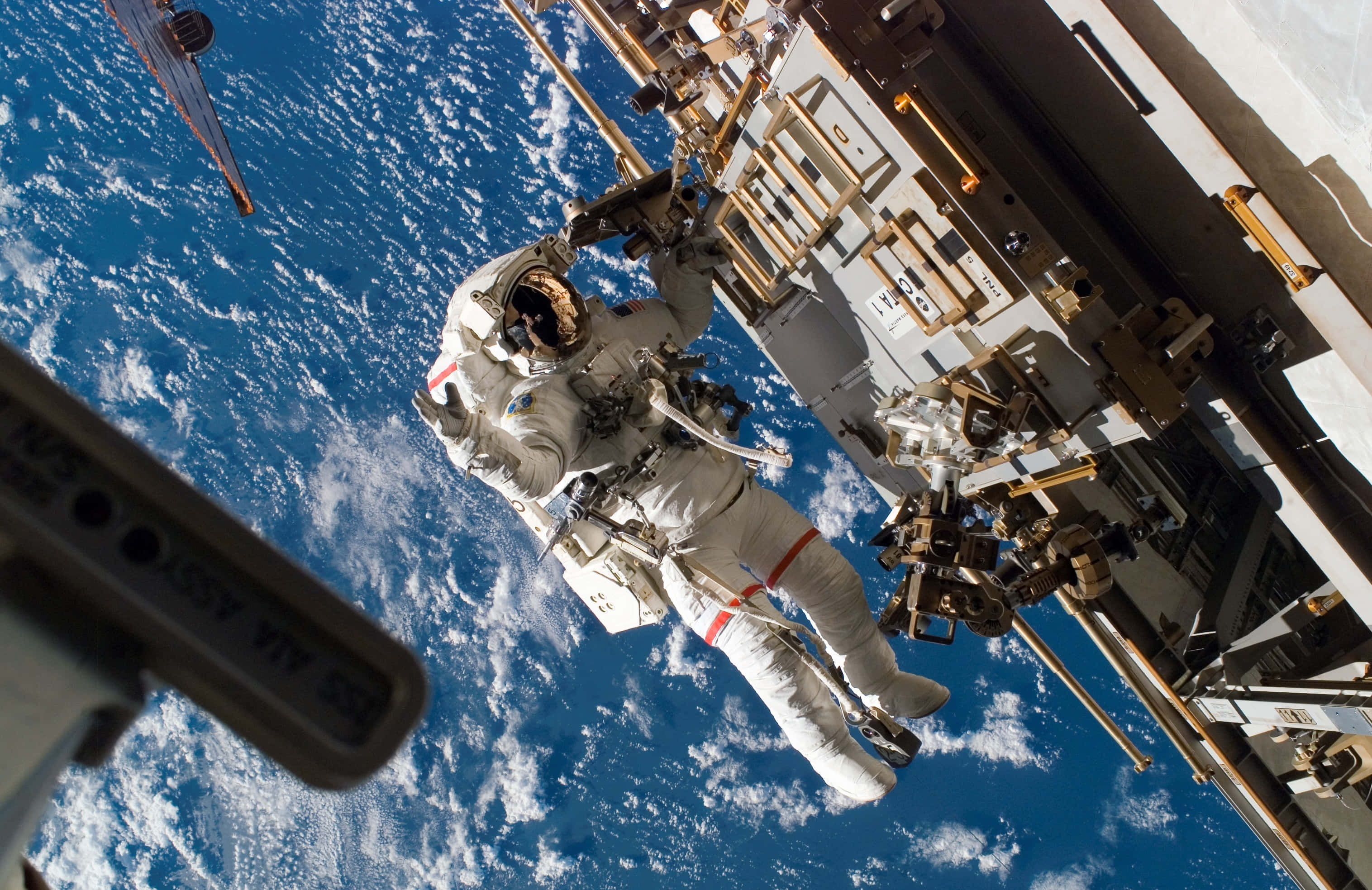 Space Station 桌布 壁紙 — 一名太空人在國際太空站外漂浮，背景是地球的藍色海洋和白色雲層。