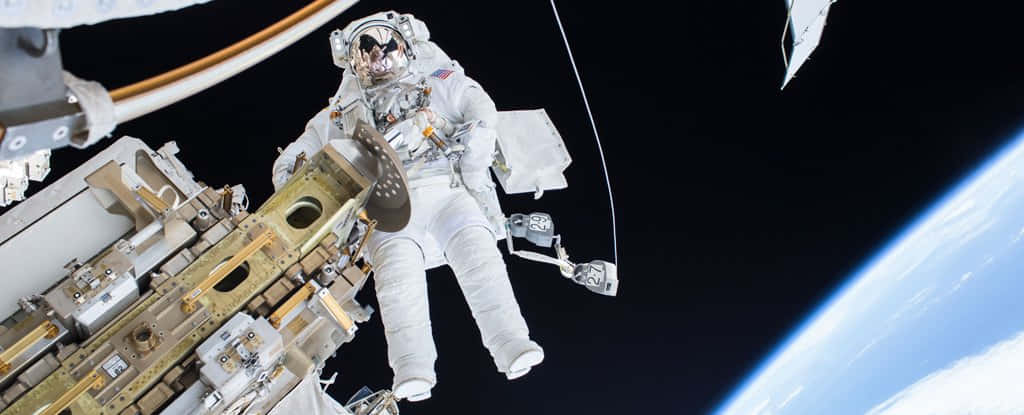 International Space Station 桌布 壁紙 — 一名太空人在國際太空站外漂浮，背景是漆黑的太空，下方是地球彎曲的藍色地平線。