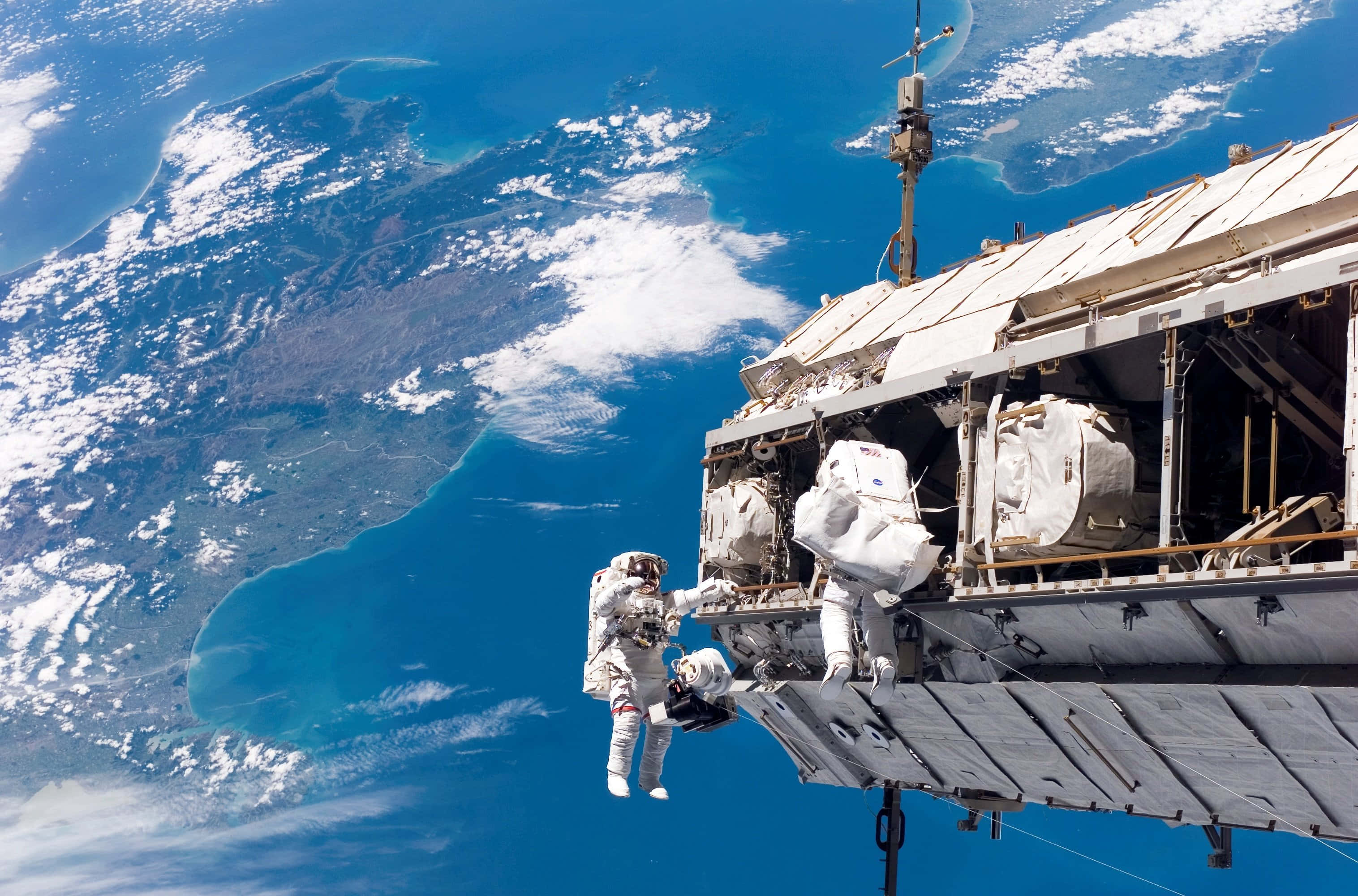 Space Mission 桌布 壁紙 — 一名太空人漂浮在國際太空站外，背景是地球充滿活力的藍色海洋和旋轉的白雲。