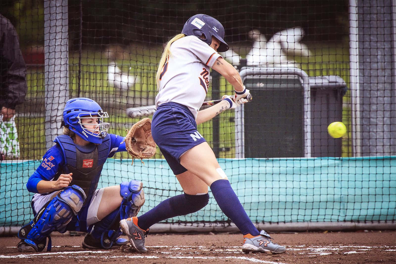 Softball 桌布 壁紙 — 一名女壘球手揮動球棒，捕手全副裝備蹲在本壘板後方。